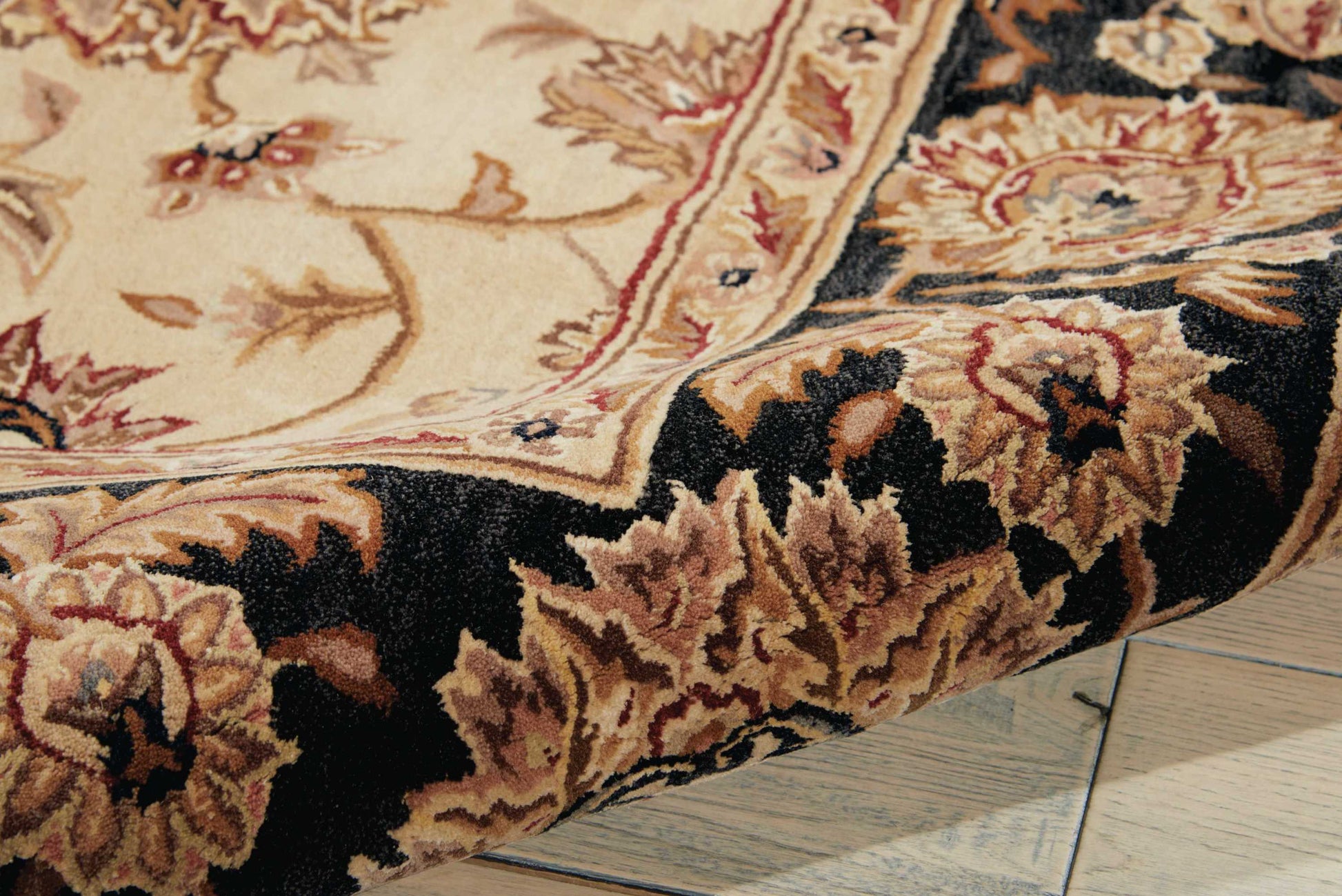 Persian-style decorative rug with cream field and burgundy floral border, dark outer edge, partly rolled on a wooden floor.