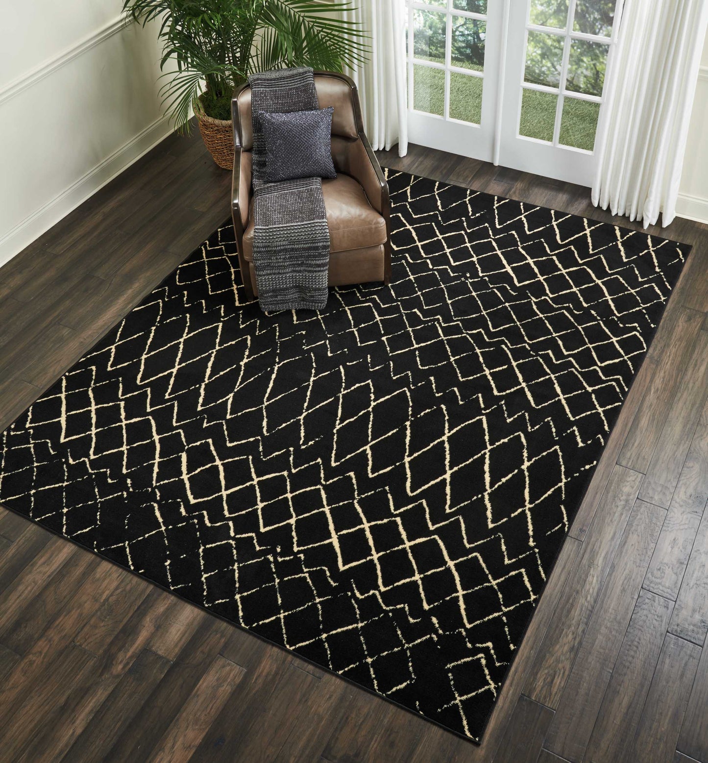 Black area rug with cream geometric lattice pattern on dark wood floor beside a brown leather armchair & gray throw