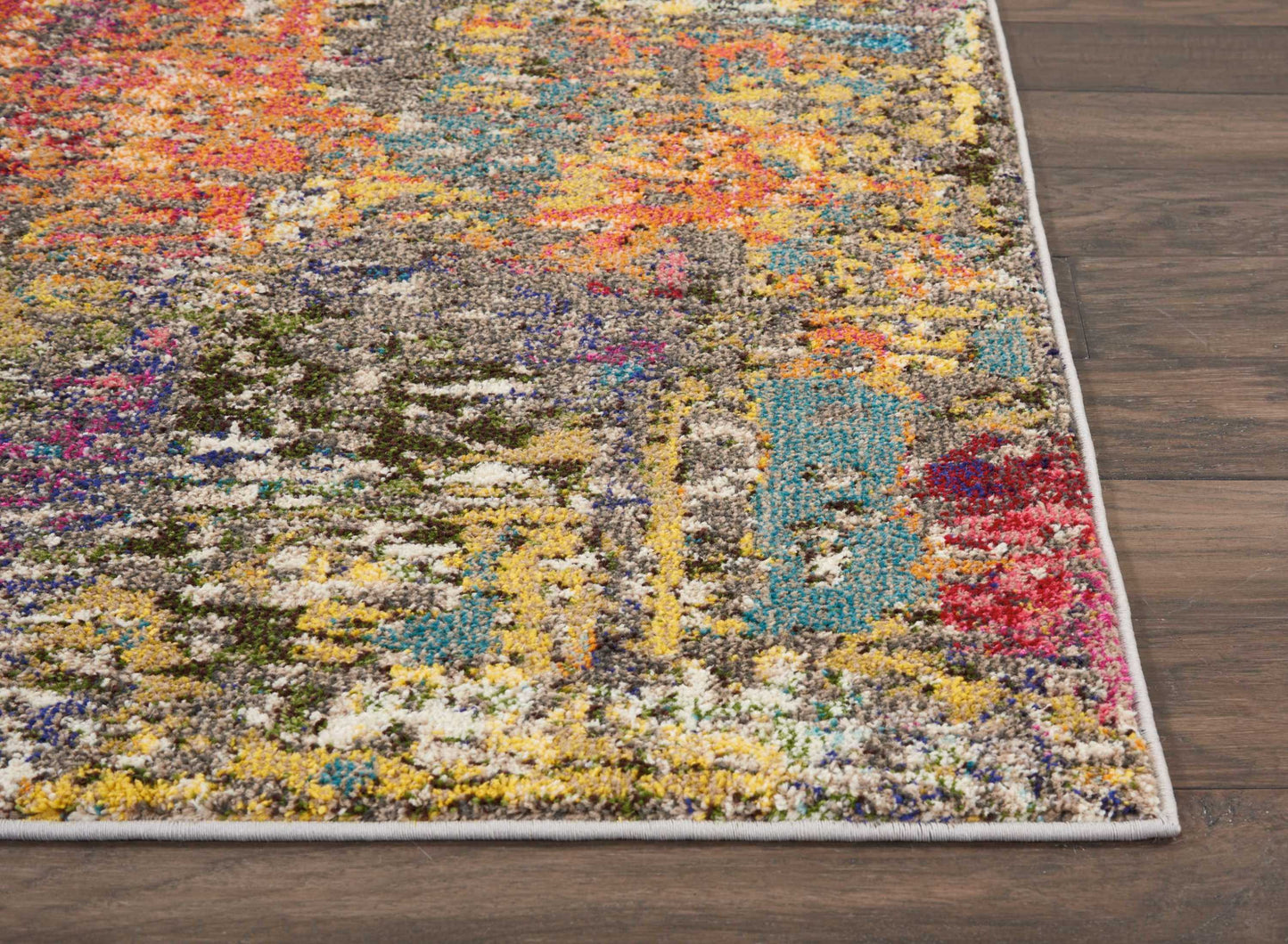 Abstract multicolor shag rug with vibrant yellows, blues, pinks and grays, light gray border on wood floor.