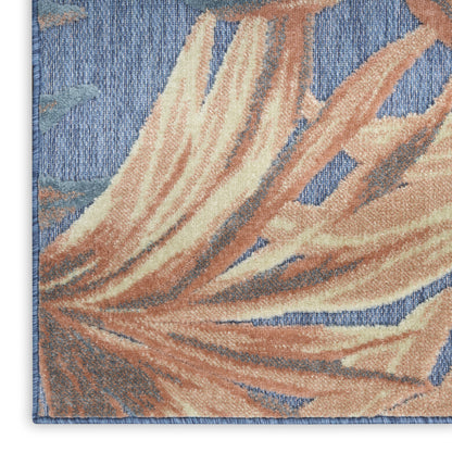 Close-up of a blue tufted rug with peach and cream palm leaf pattern and bound edge.