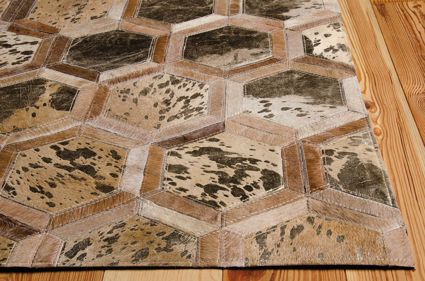 Cowhide patchwork hexagon rug in brown, tan and beige with cream stitching on a wooden floor.