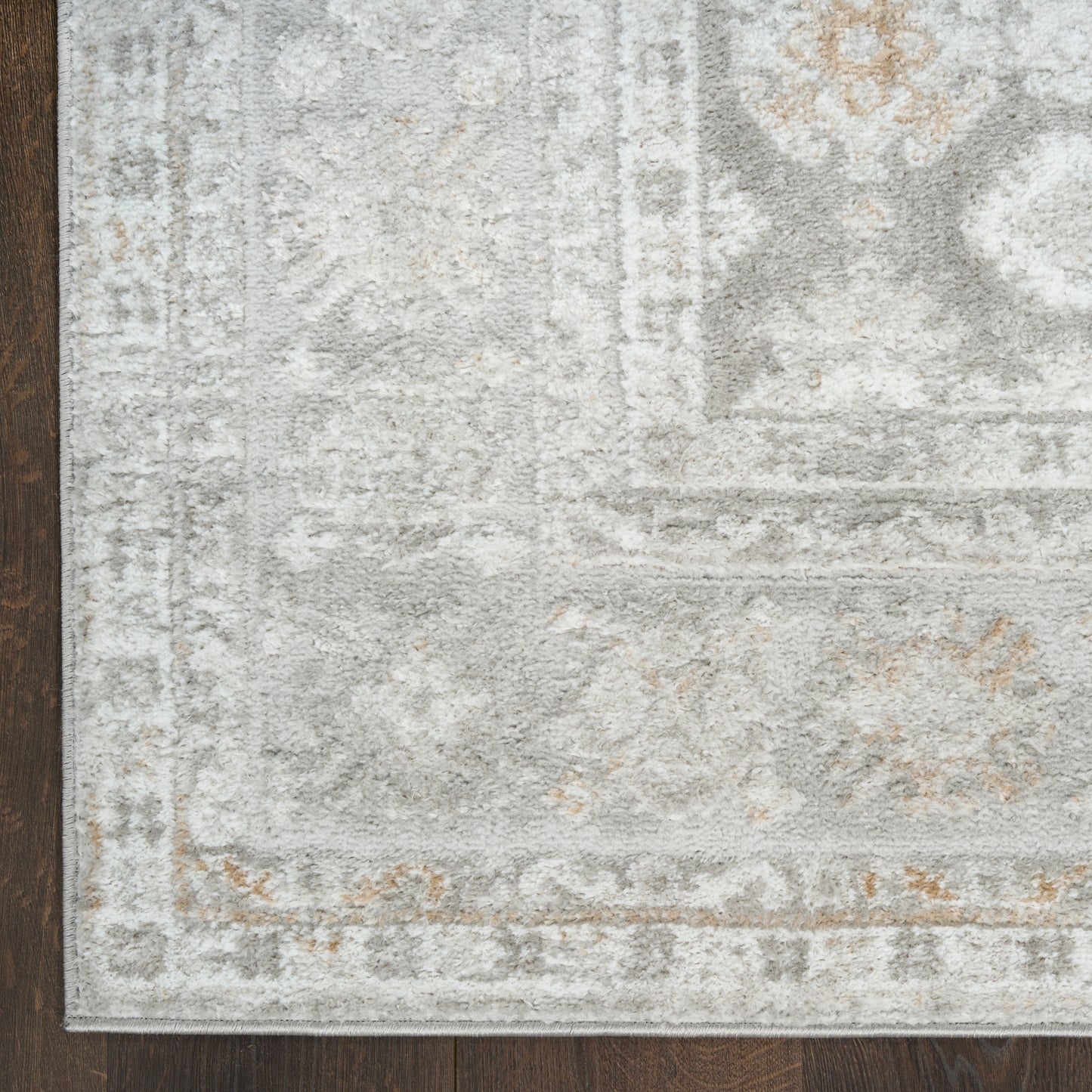 Soft, plush light gray area rug with ivory distressed pattern and tan accents on a dark wooden floor.
