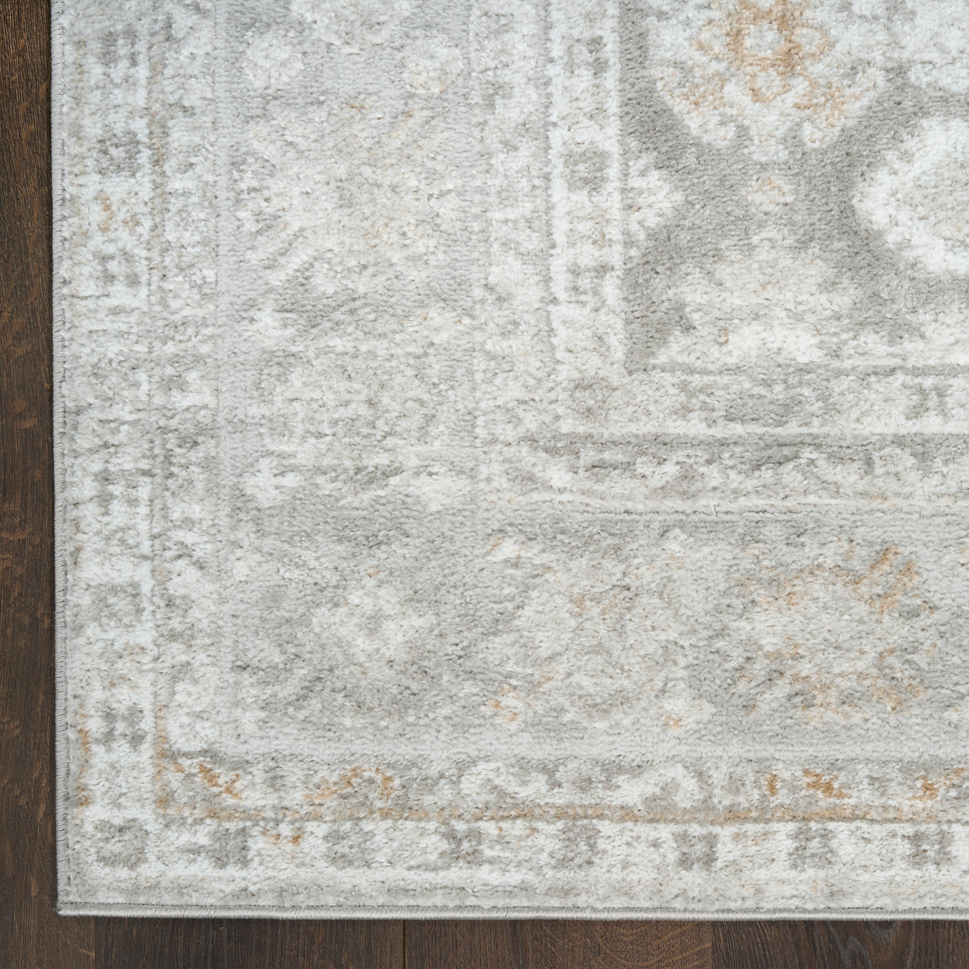 Soft, plush light gray area rug with ivory distressed pattern and tan accents on a dark wooden floor.