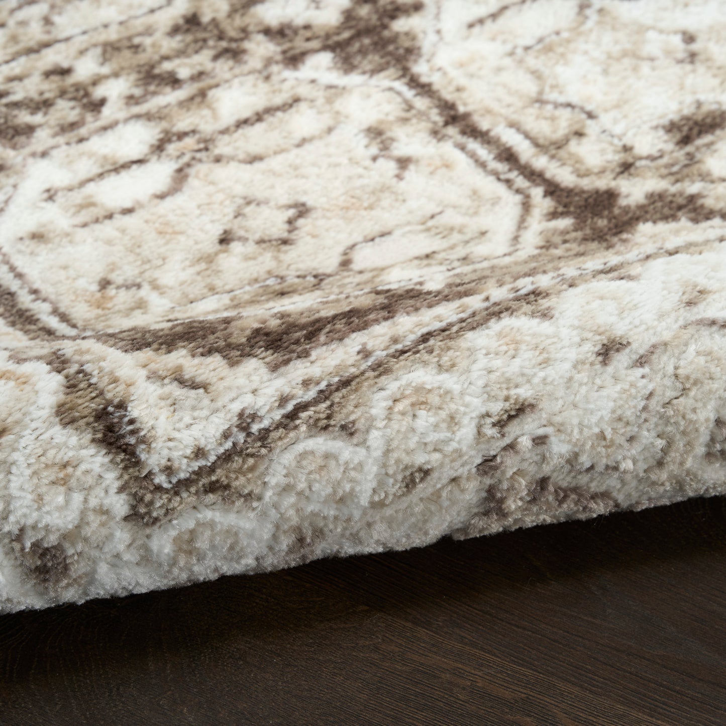 Thick beige cream shag rug with brown ornate border pattern on dark wood floor.
