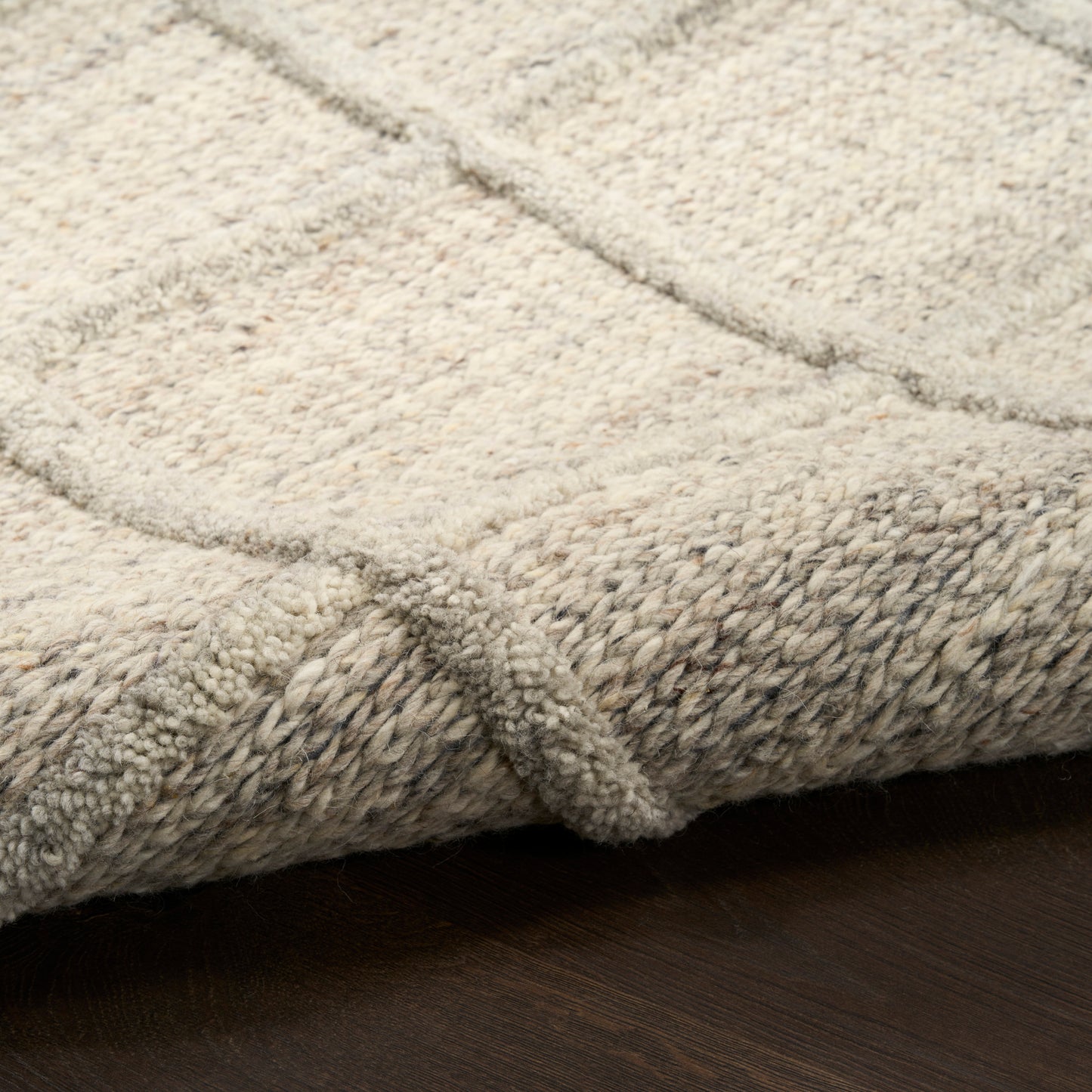 Cream beige rug with loop-pile texture and braided edge resting on dark wood floor.