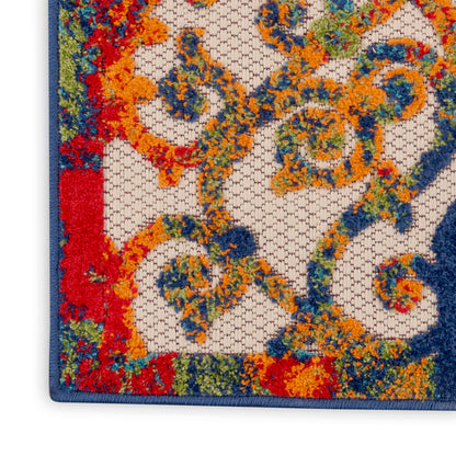 Colorful ornate rug corner with blue border, featuring orange, yellow and blue floral scroll pattern on light background.