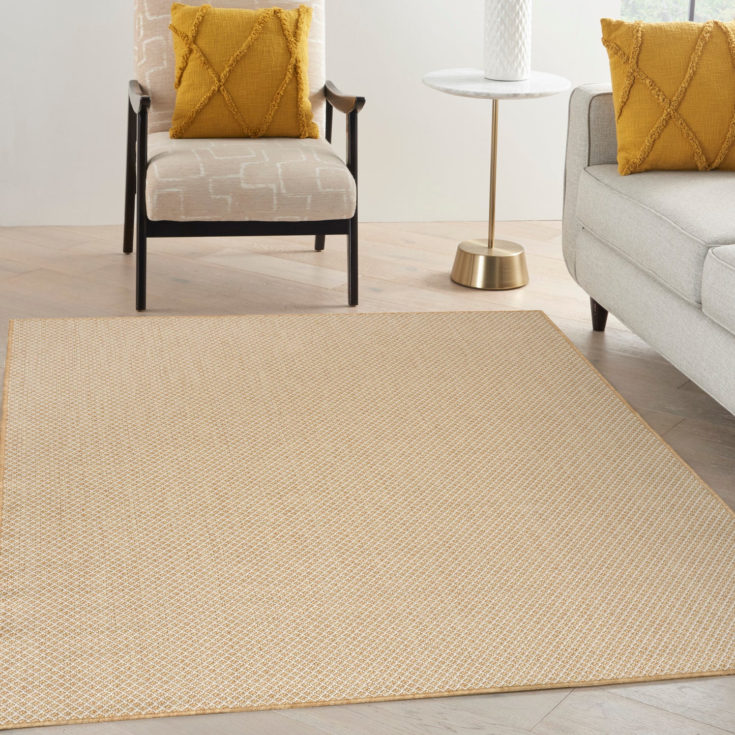 Rectangular beige woven rug in a bright living room with mustard pillows on beige armchair and gray sofa, gold side table.