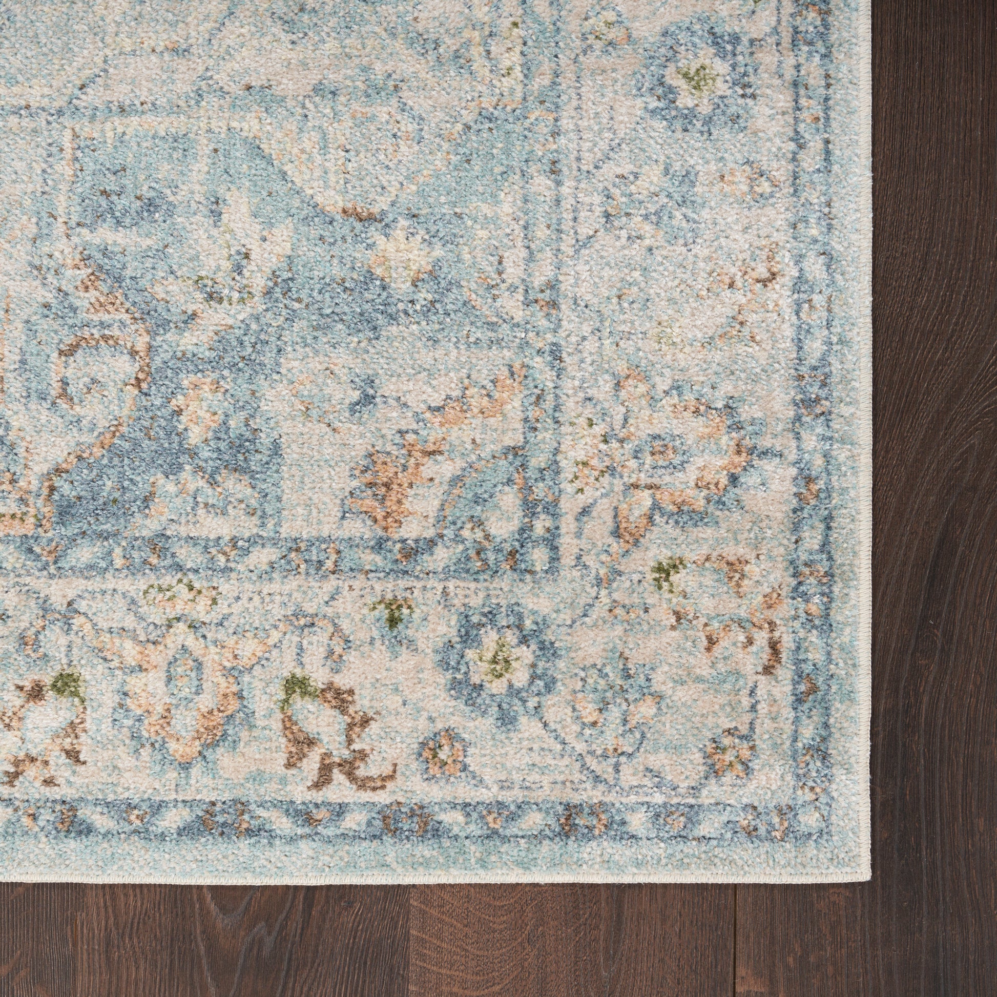 Blue and ivory ornate rug corner with floral motifs on dark wood floor.