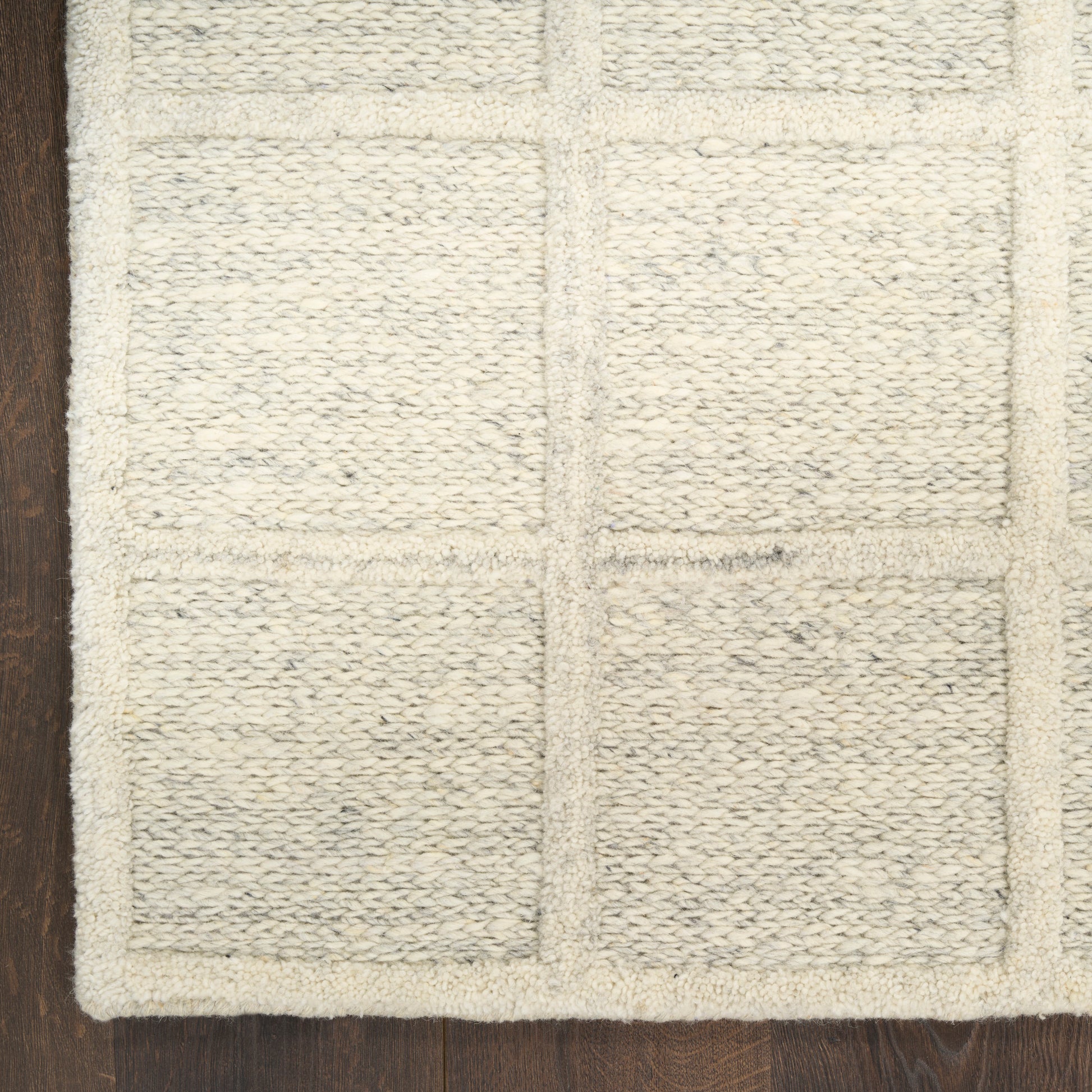 Cream bath mat with rectangular patchwork blocks, woven textured loops, plush cotton on dark wooden floor.