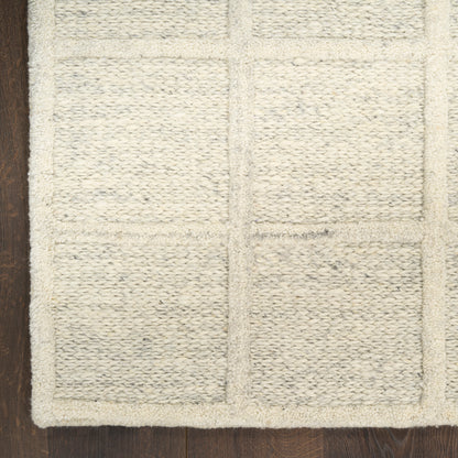 Cream bath mat with rectangular patchwork blocks, woven textured loops, plush cotton on dark wooden floor.
