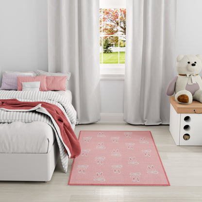 Soft pink bunny-pattern rug in a pastel kids' room with gray bedding, white curtains, and a teddy on a white nightstand.