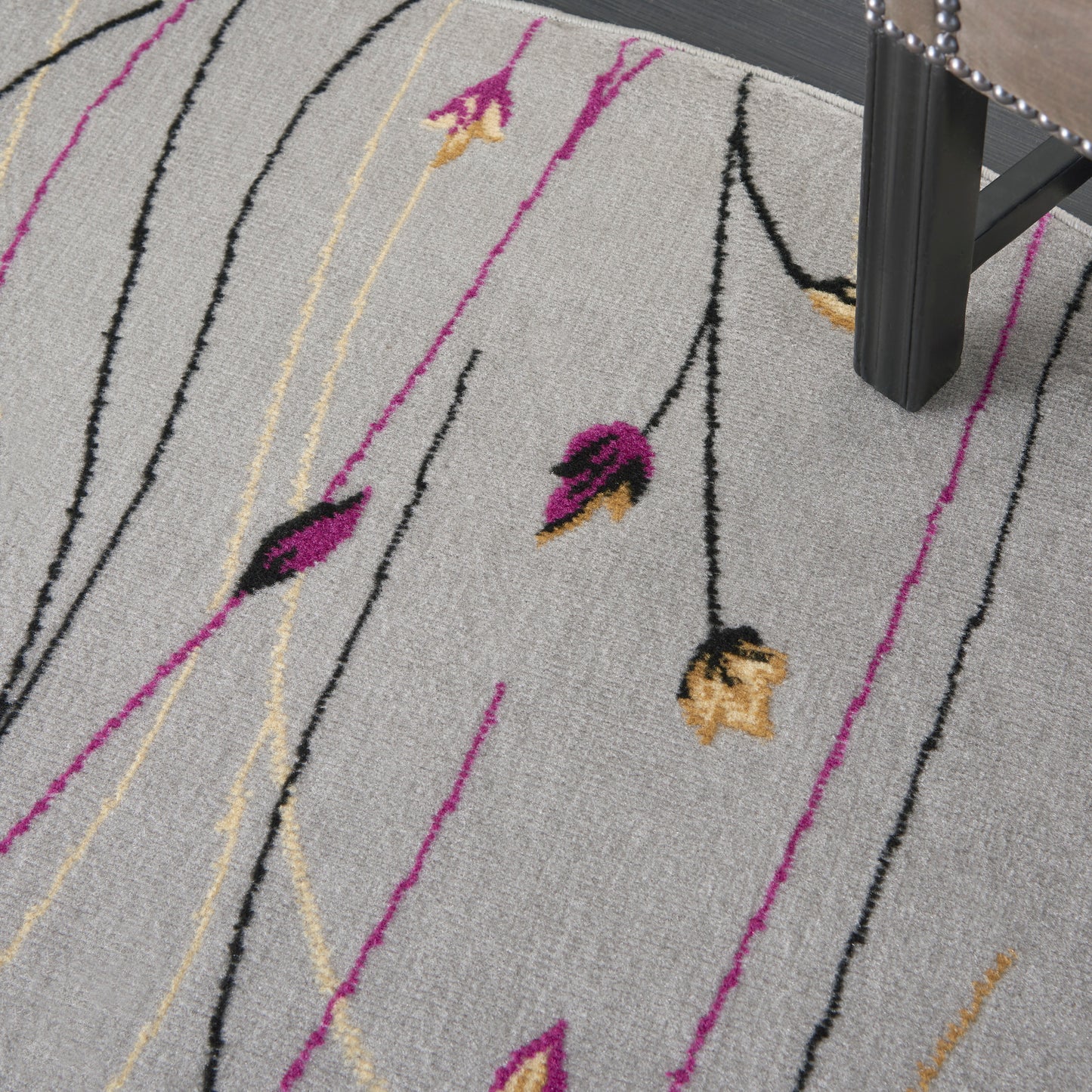 Light gray rug with abstract magenta, black and yellow floral lines; modern area rug under a chair.