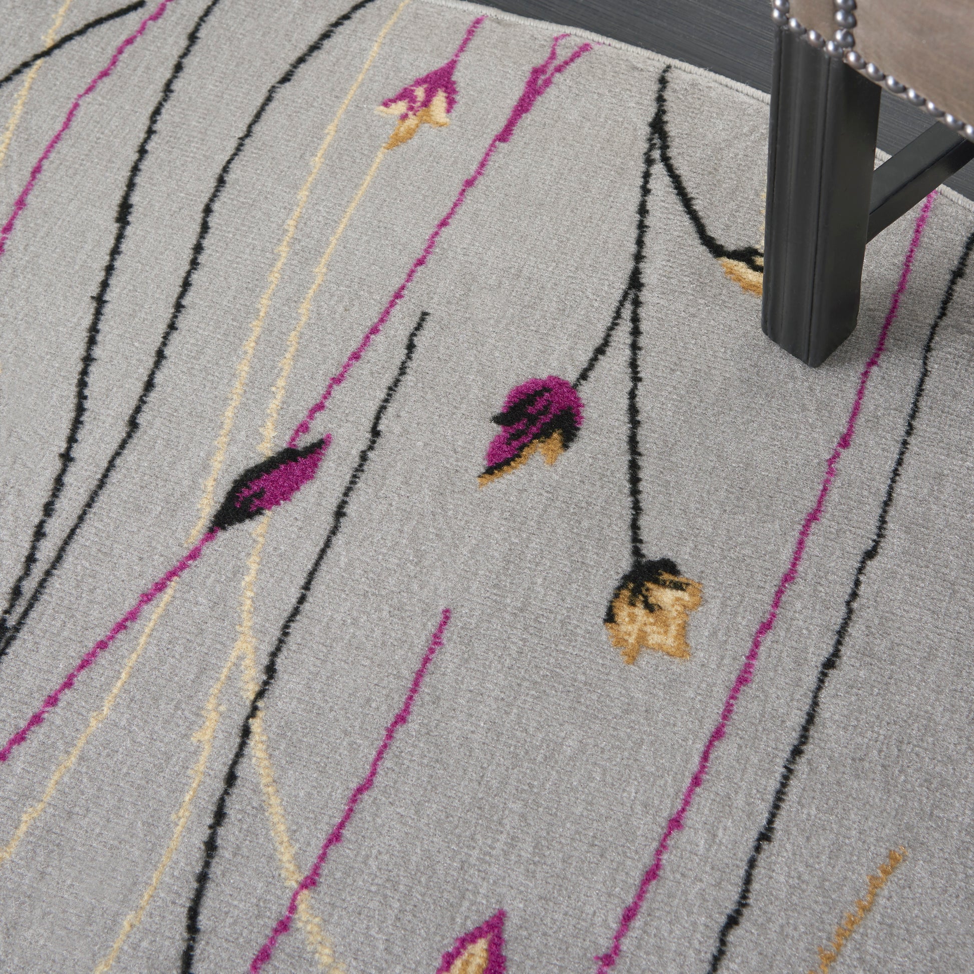 Light gray rug with abstract magenta, black and yellow floral lines; modern area rug under a chair.