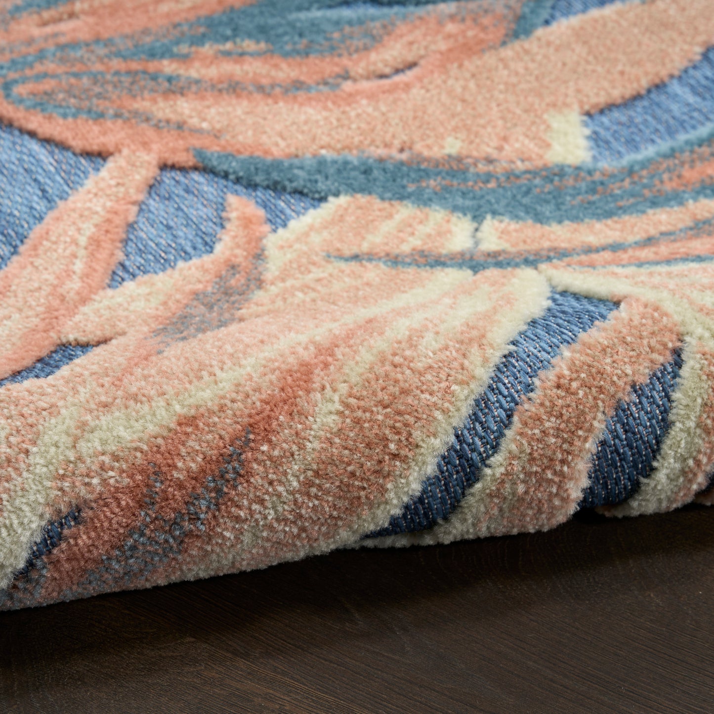 Soft peach, blue and cream abstract rug with plush thick pile, folded edge on dark wood floor.