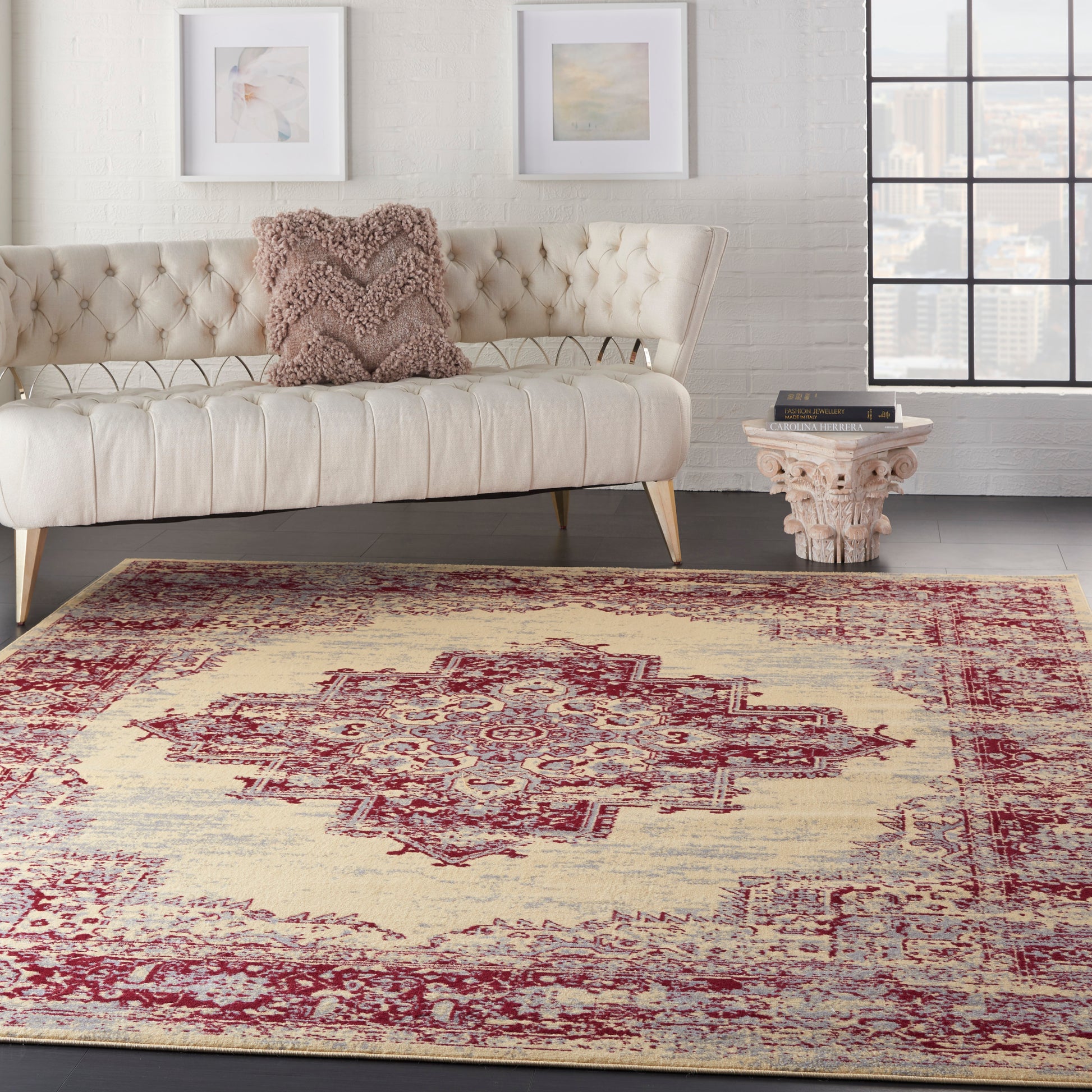 Vintage red patterned rug 7' x 10' on a floor in a living room scene with cream tufted sofa, pale legs, white brick wall, framed art and carved table.