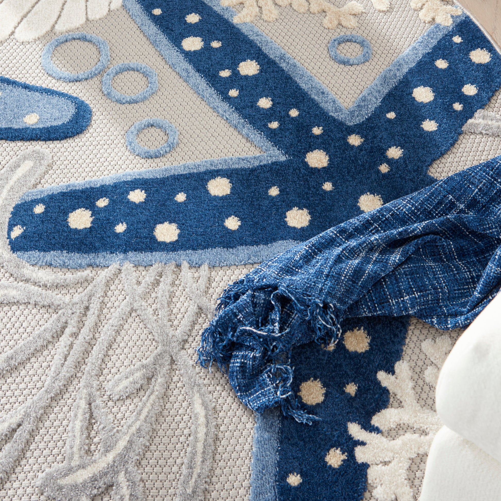 Denim-blue fabric roll with a frayed edge resting on a textured cream rug featuring blue dotted circles.