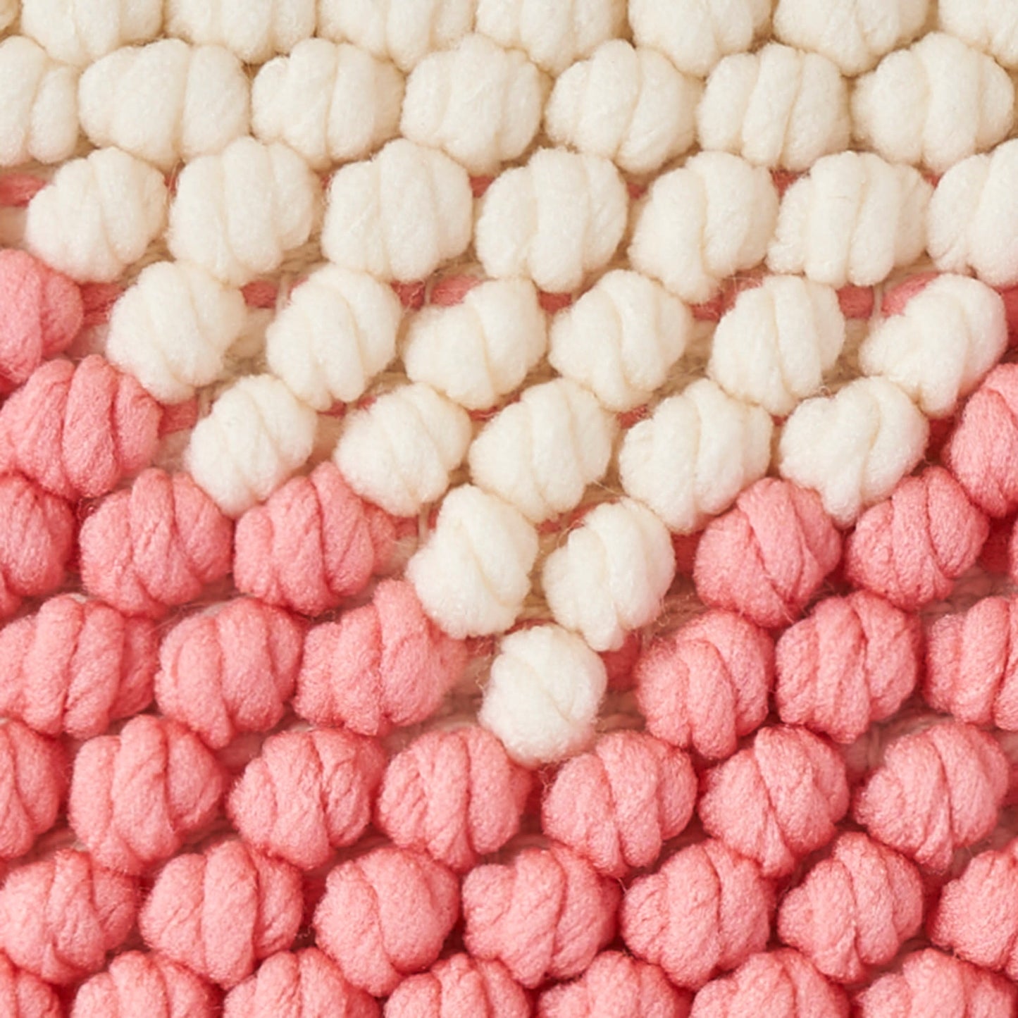 Close-up of chunky pom-pom yarn knit in ivory to pink gradient, cozy textured pillow.