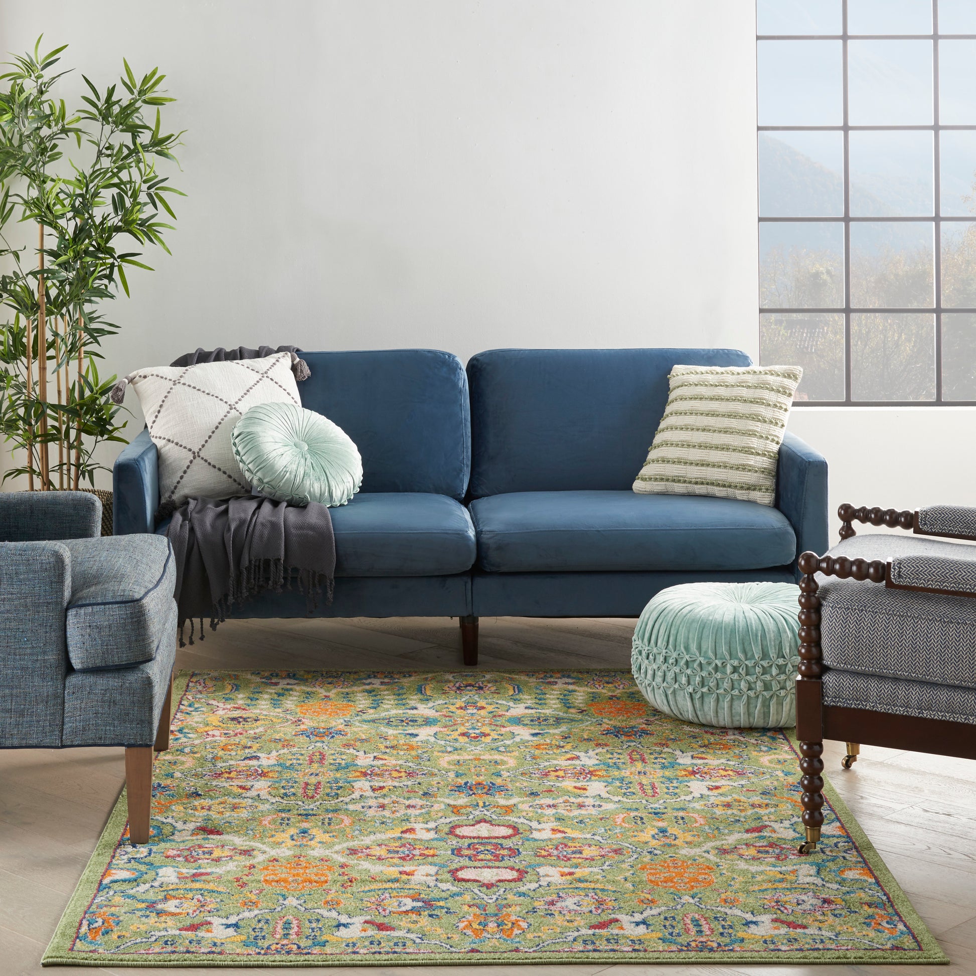 Blue velvet sofa, mint pouf, and a colorful patterned rug, 4' x 6', in a bright living room with a leafy plant.