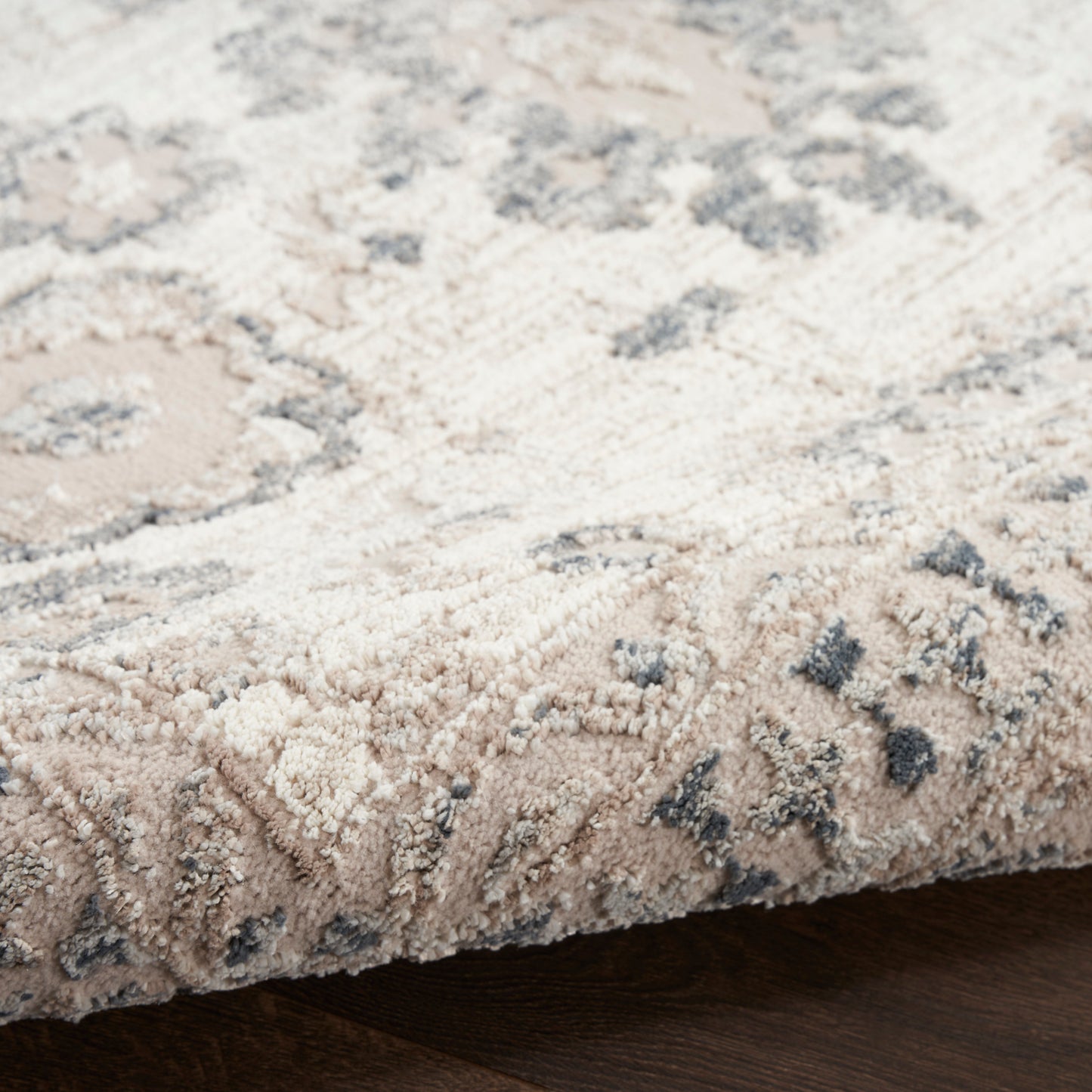 Beige and gray floral-patterned area rug with plush pile on dark wood floor.