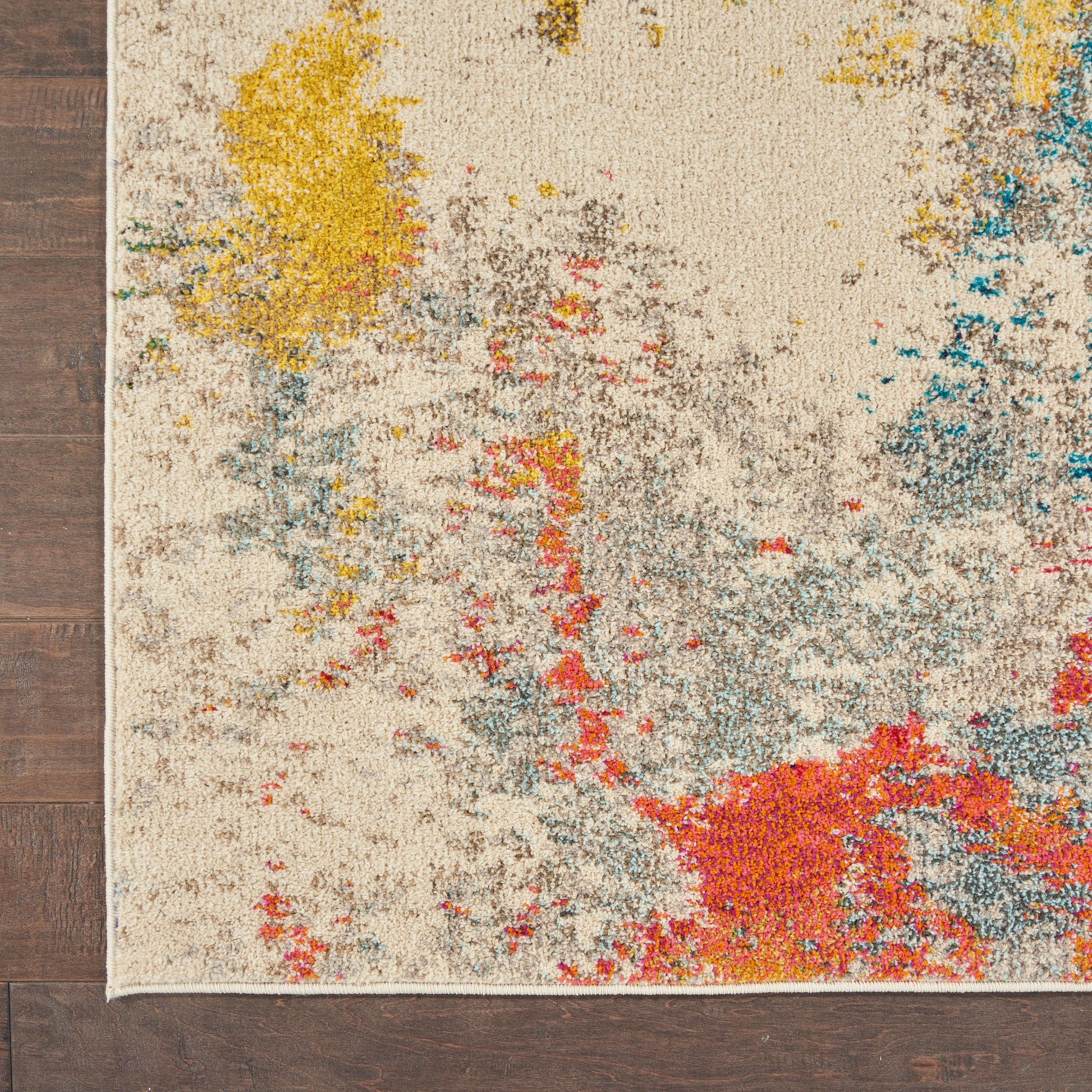 Cream rug with abstract multicolor splashes (yellow, red, blue, gray) and fringed edge on dark wood floor.