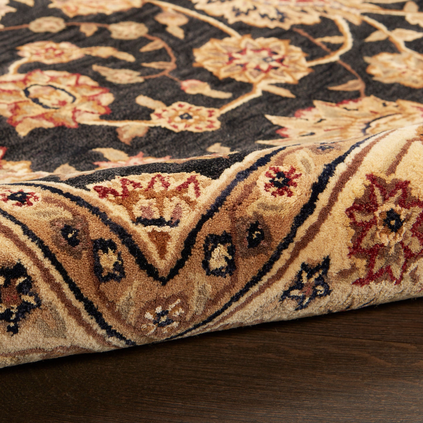 Persian-style area rug with dark navy field, beige/gold floral border and red accents on a wooden floor.