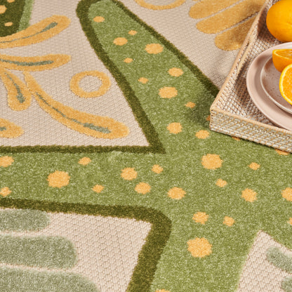 Green cactus-pattern outdoor rug with yellow polka dots on beige; wicker tray with orange slices on top.