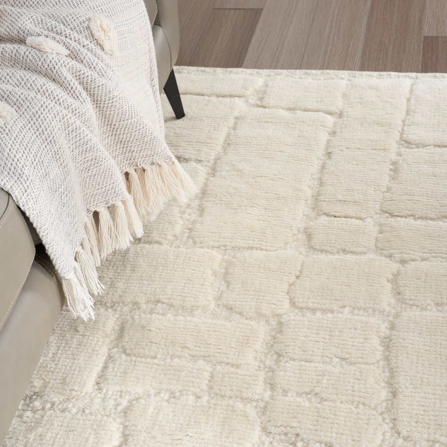 Cream shag rug with square grid texture in a living room, draped beige knit blanket on sofa, wooden floor.