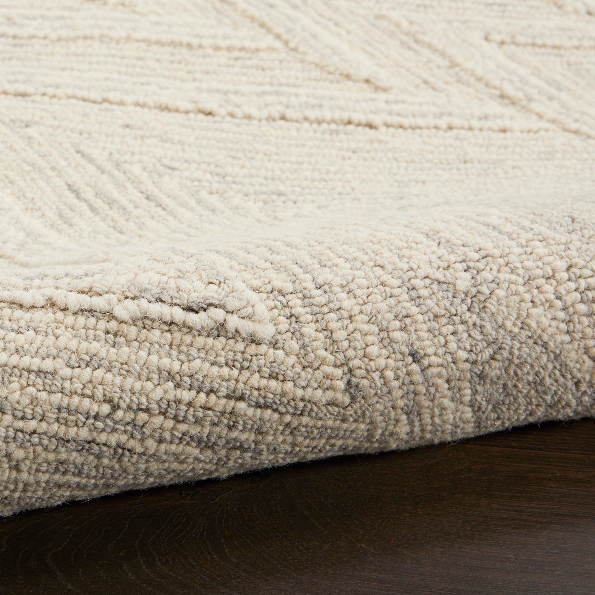 Beige textured area rug with boucle pile and subtle geometric pattern on dark wood floor.
