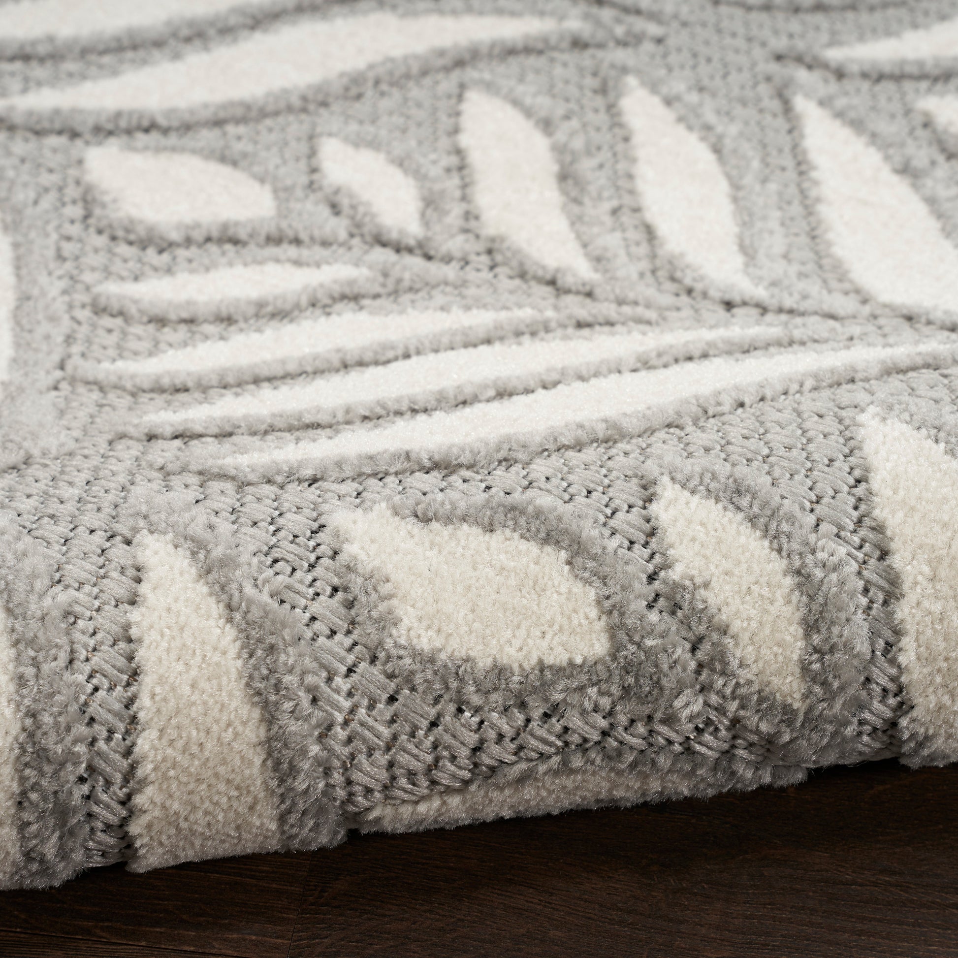 Grey and ivory patterned rug with leaf motif, plush pile on dark wood floor.