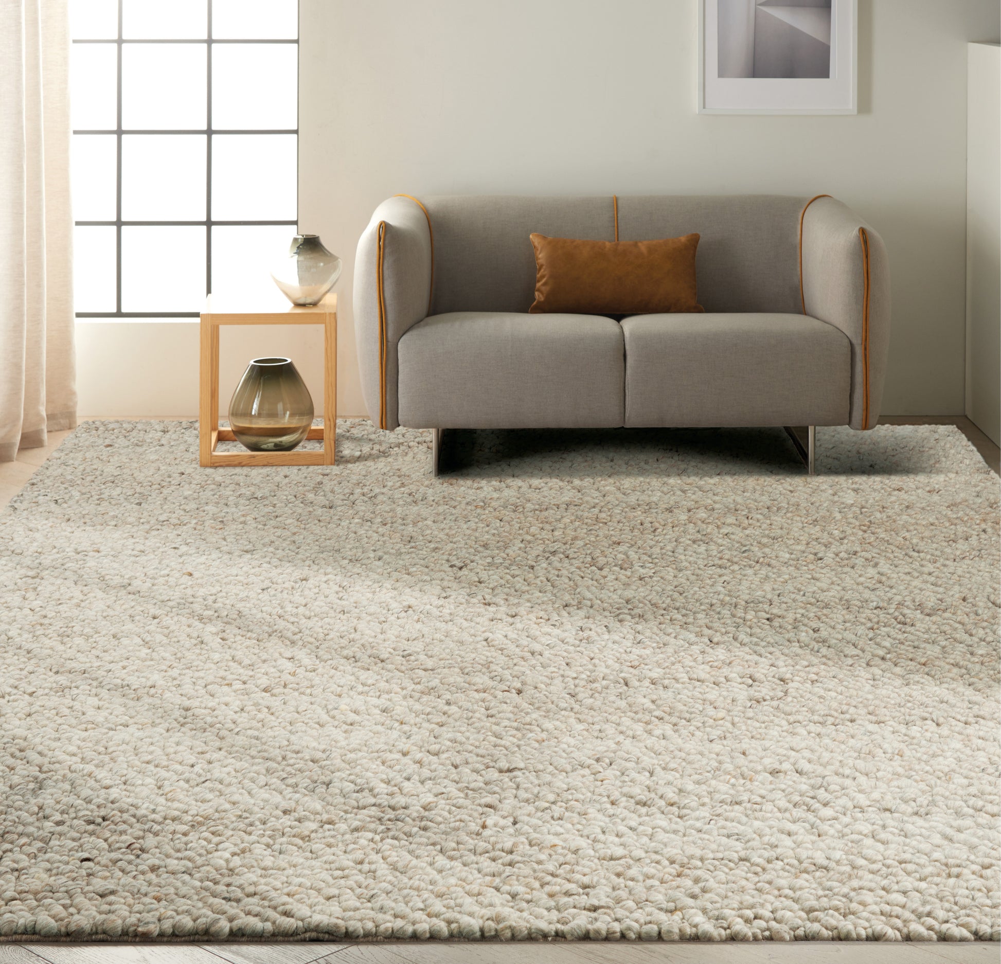 Light grey 2-seat sofa with orange piping and brown cushion, on a cream shag rug beside a wooden side table with vases.