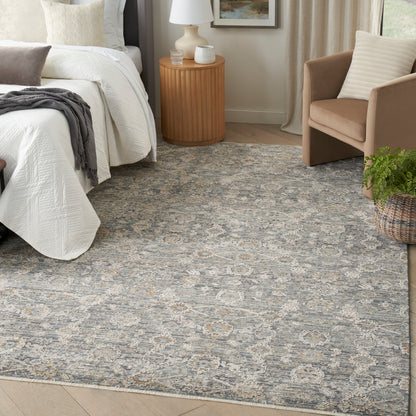 Gray-blue patterned area rug with beige motifs in a cozy bedroom, white bed, round nightstand, and beige armchair.
