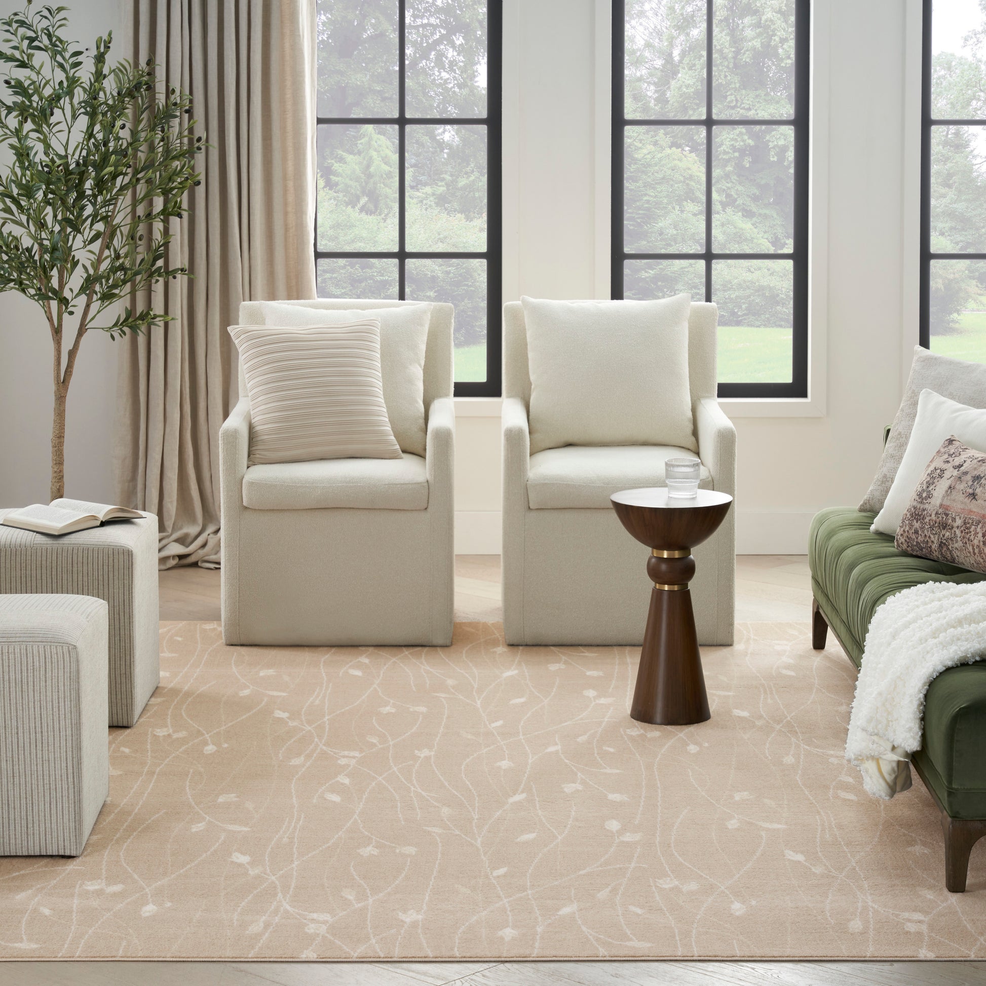 Cream armchairs, beige patterned rug, wooden side table, green sofa, tall plant, and large black-framed windows.