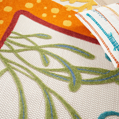 Close-up of colorful woven fabrics: orange patterned section, green vine embroidery on beige mesh, and a striped rolled towel with blue and orange lines.
