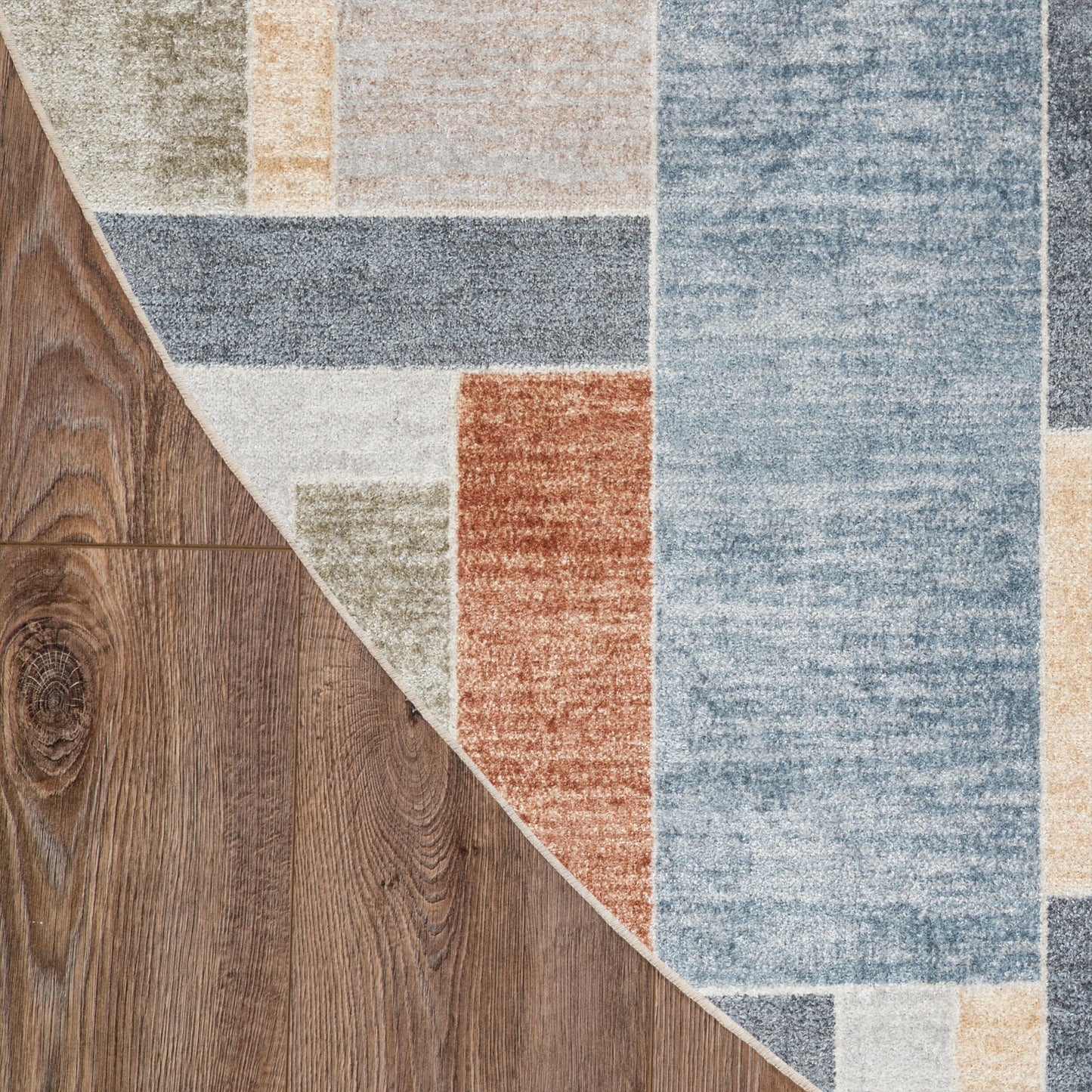 Patchwork round rug with blue, beige, gray and orange blocks; low-pile texture, curved dark wood floor visible around the rug.