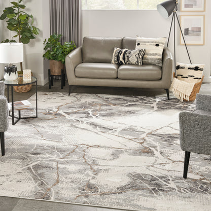 Taupe faux-leather sofa with black tapered legs in a modern living room, atop a gray abstract rug with plants, decorative cushions, and a tripod floor lamp.