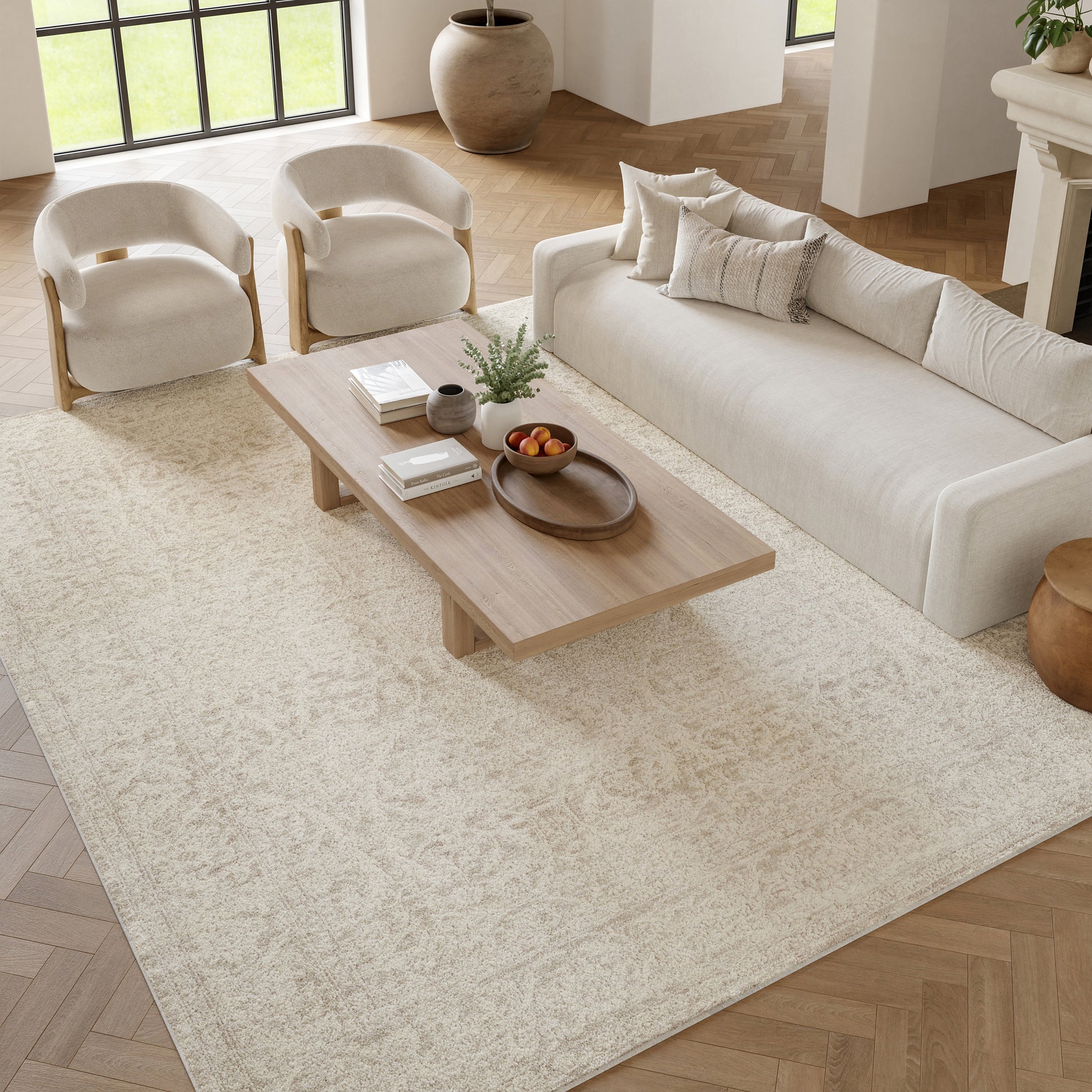 Neutral living room with cream sofa, rounded wood-arm chairs, low wooden coffee table, beige rug.