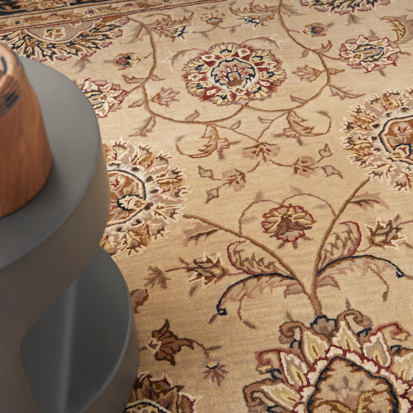 Beige traditional oriental rug with red and blue floral medallions; gray round table base partially visible