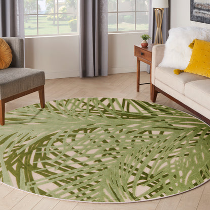 Round green palm-pattern area rug in a bright living room with beige sofa, yellow cushions, and wooden furniture.