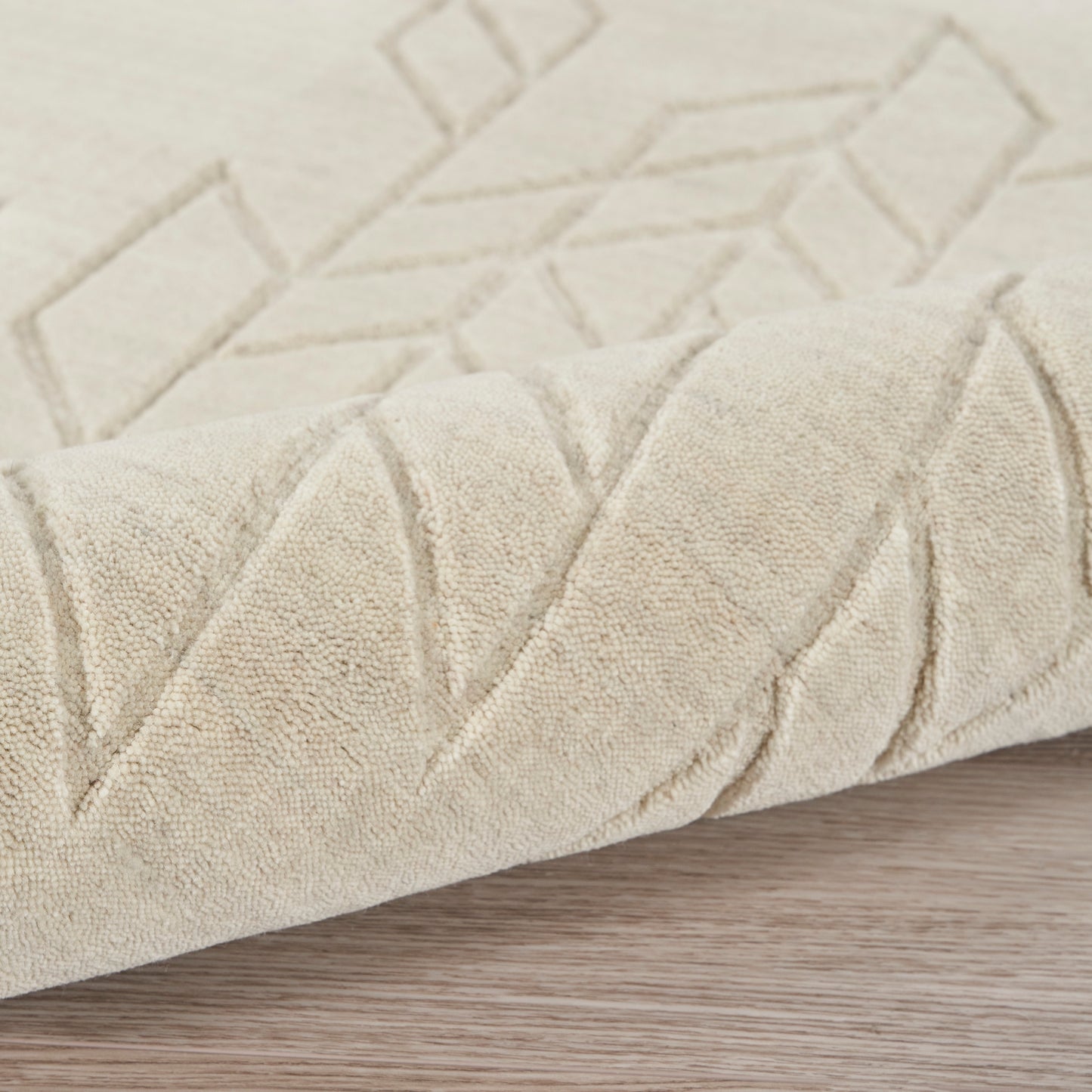 Beige geometric rug with raised chevron pattern, soft plush pile, rolled edge on light wood floor.