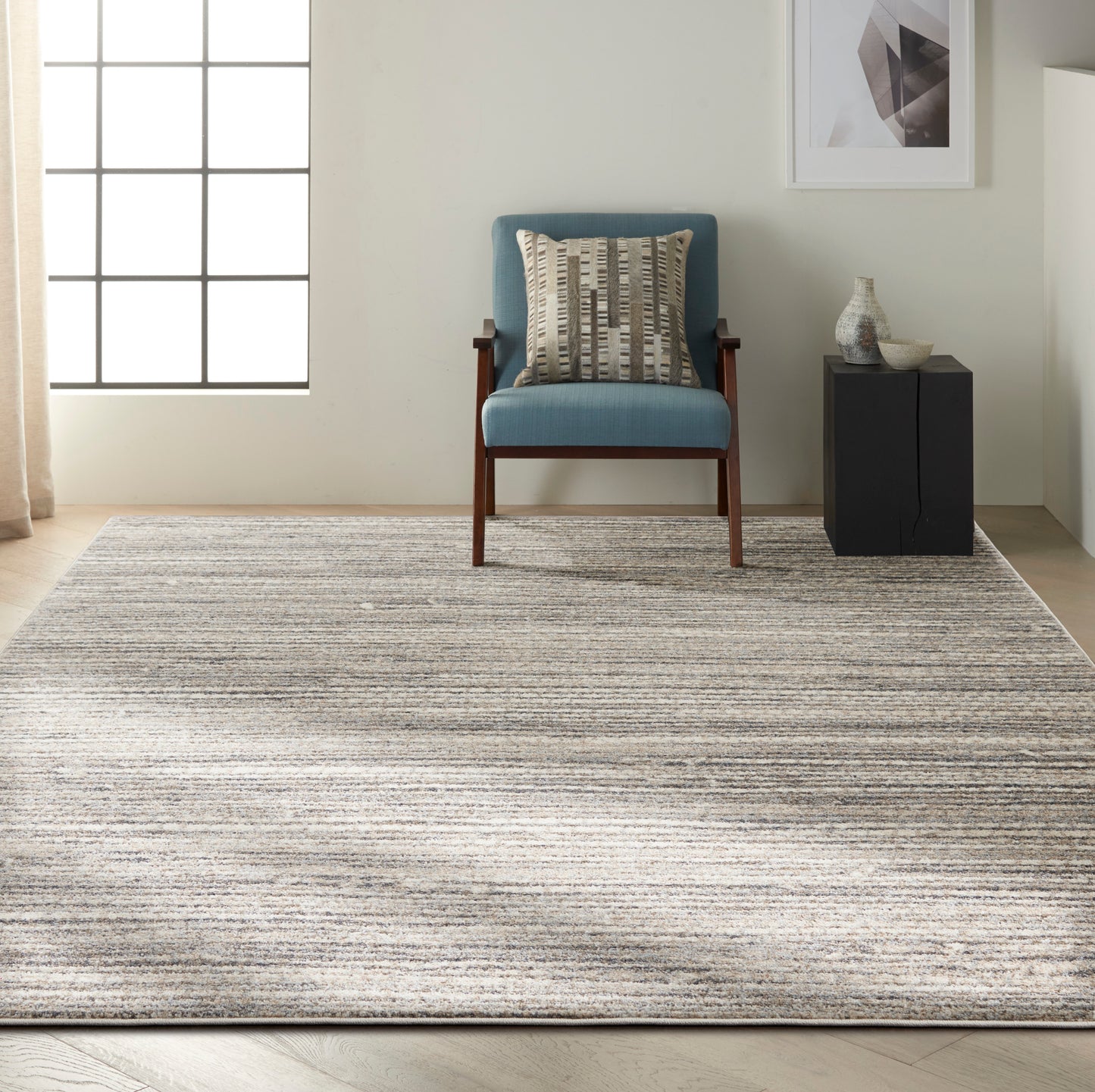 Beige striped rug with blue accents, shown with a black side table and vase.
