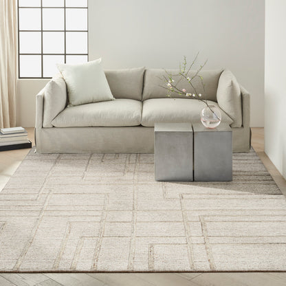 Neutral living room: light gray fabric sofa, beige rug, square concrete block coffee table, glass vase with branches.