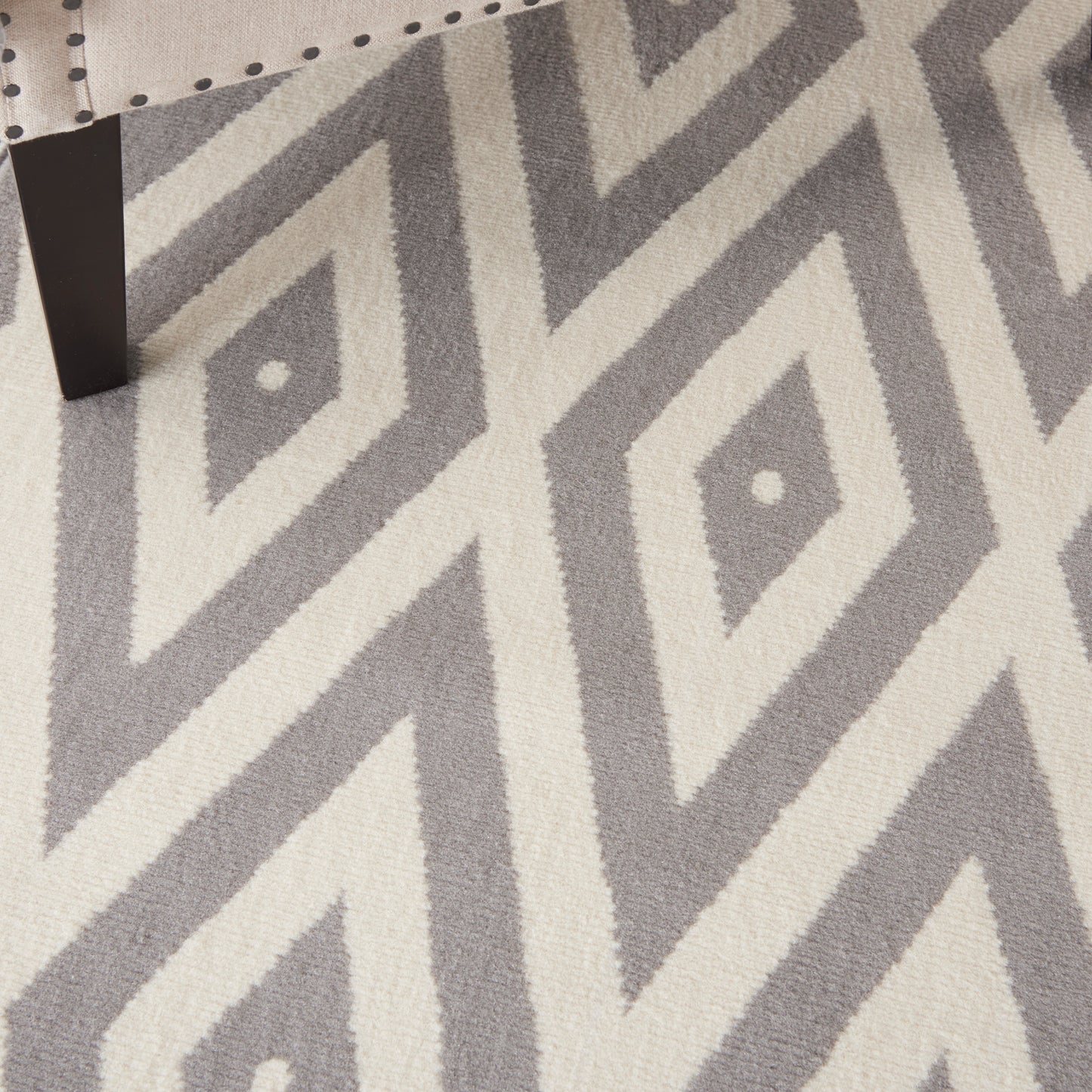Close-up of a grey and ivory geometric diamond rug with tufted pile (5' x 7'); partial dark table leg in the corner.