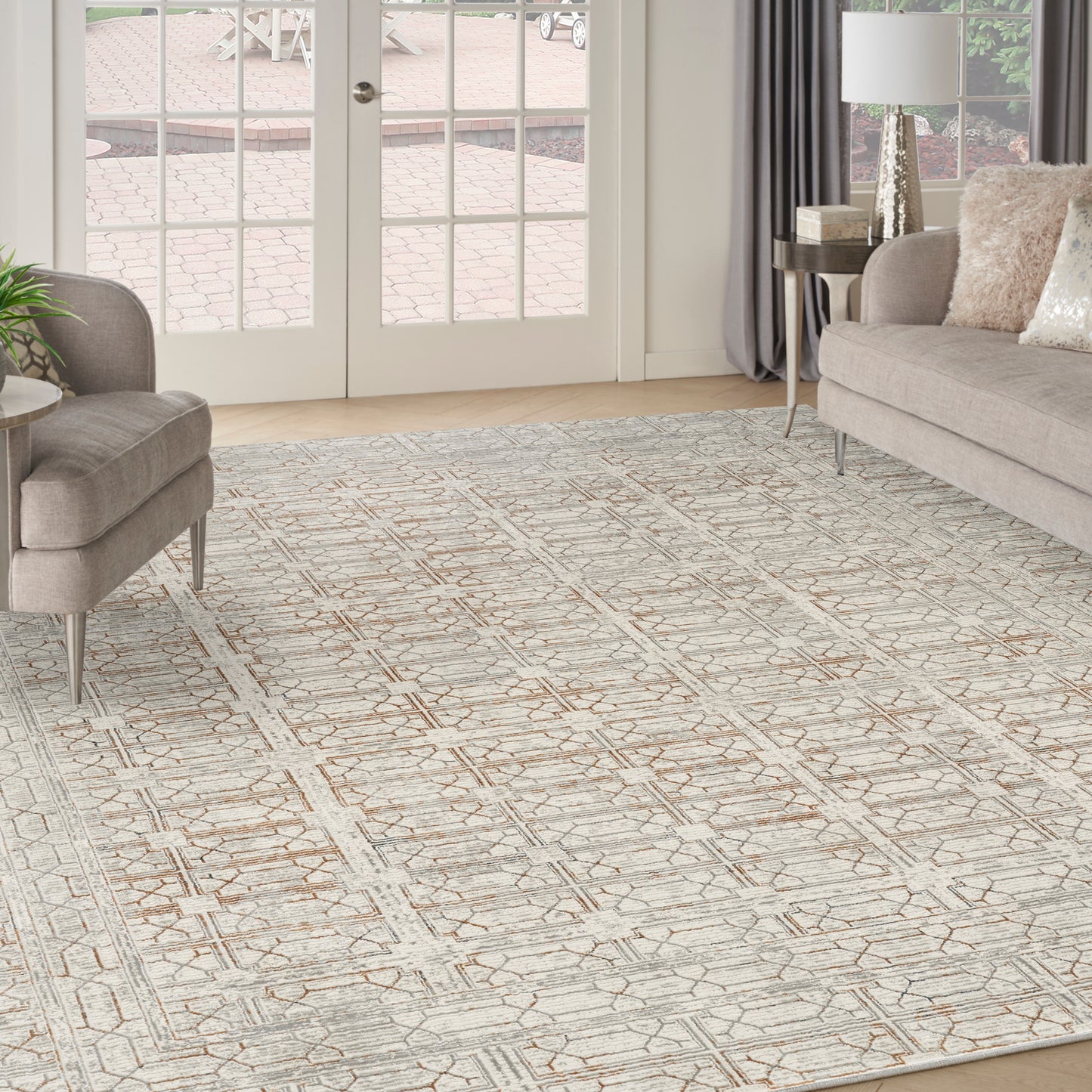 Neutral geometric area rug in cream & tan, in a modern living room with beige sofa, ottoman, & glass doors.
