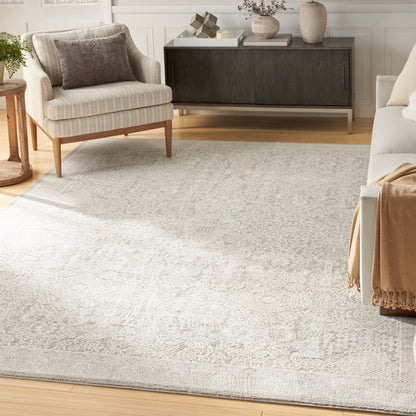 Neutral living room with a pale gray patterned area rug, beige armchair, dark wood console, light wood floors, cozy throw.