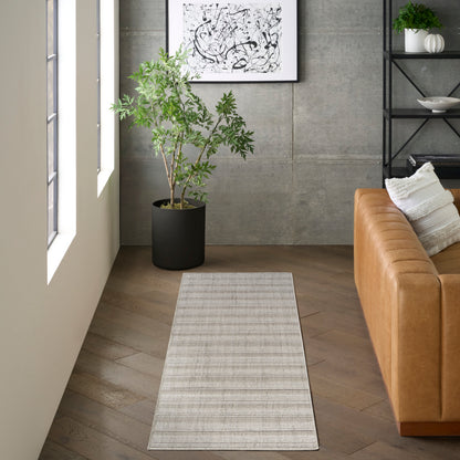 Light gray woven runner rug on wooden floor beside a tan leather sofa, potted plant, abstract art & black metal shelving.