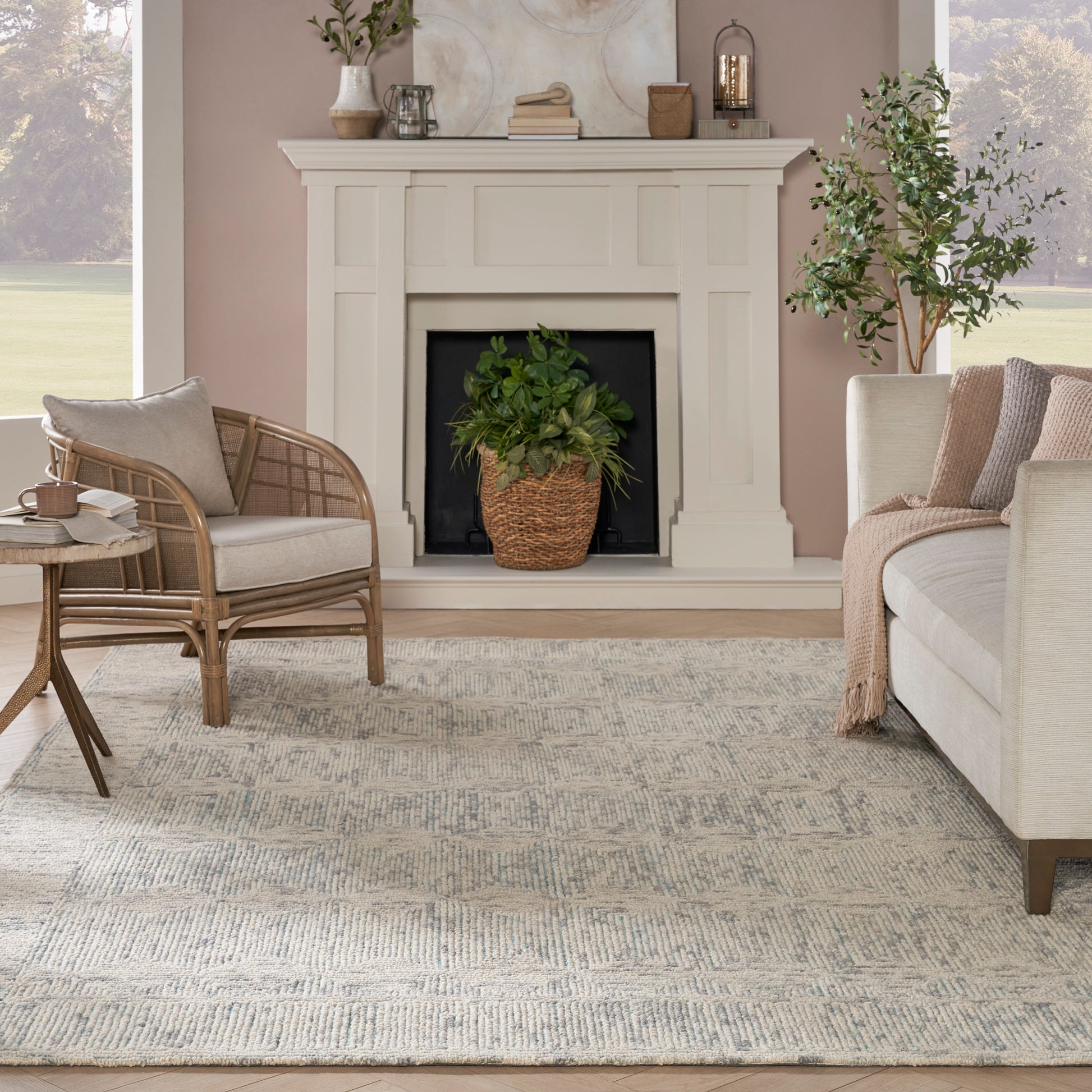 Cozy living room with white mantel fireplace, mauve walls, wicker chair, beige sofa, woven basket plant, wood table, rug.