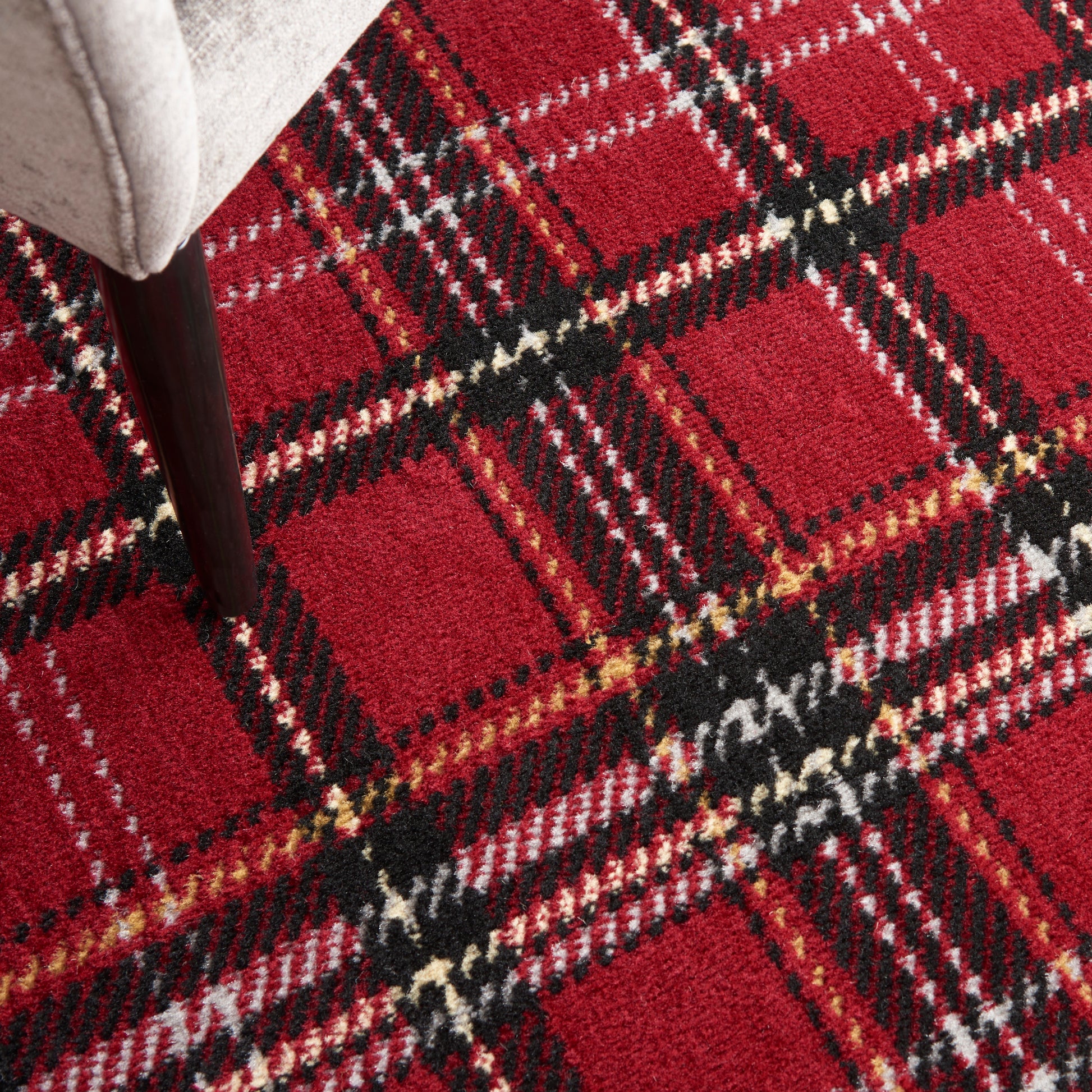 Red plaid rug with black, white and yellow lines; chair leg resting on it.