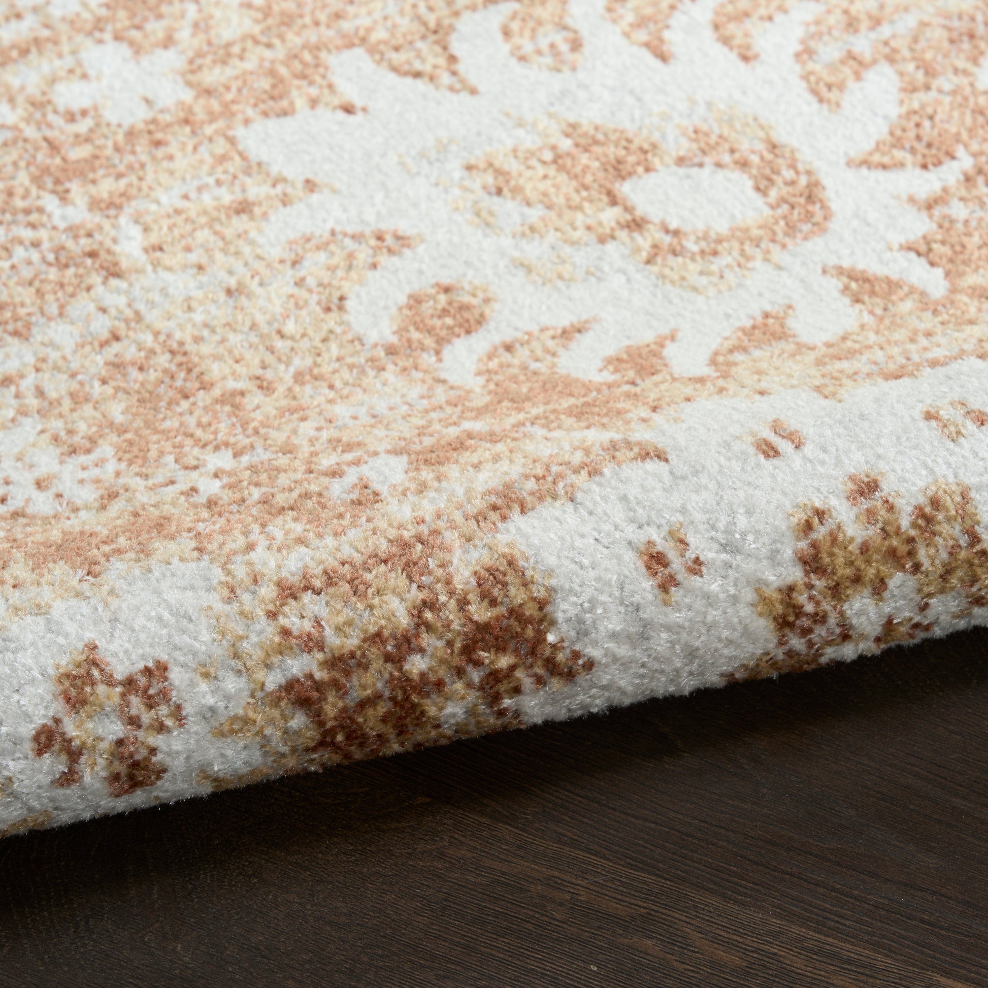 Soft plush rug in peach and ivory floral medallion, thick pile; folded edge on dark wood floor.