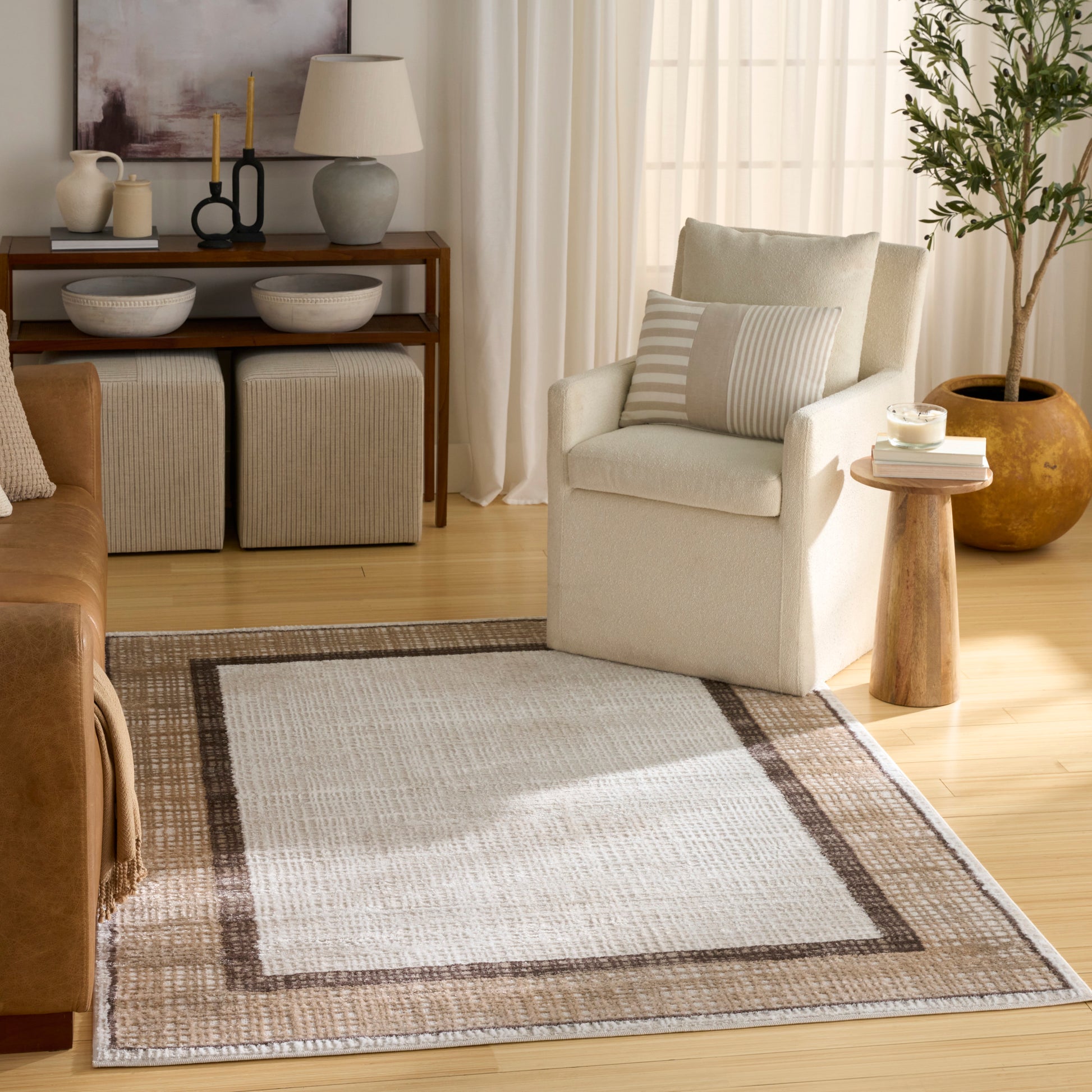 Neutral living room with cream armchair, striped cushion, beige woven rug with brown border, wooden side table, potted plant.