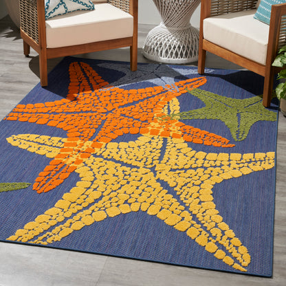 Outdoor woven rug with oversized orange and yellow starfish on navy blue background between wicker chairs.